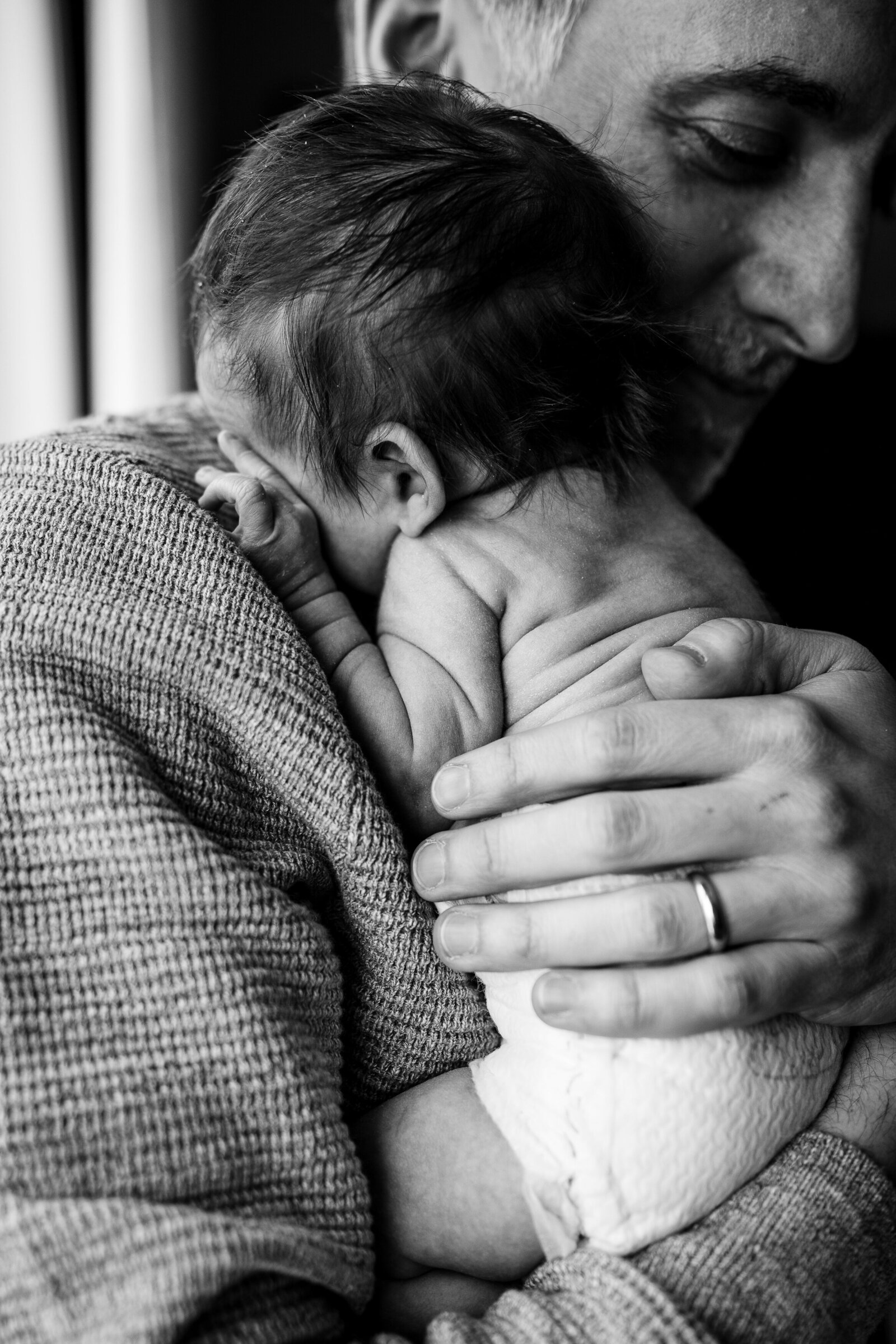 black and white photo of dad holding wrinkly baby to chest