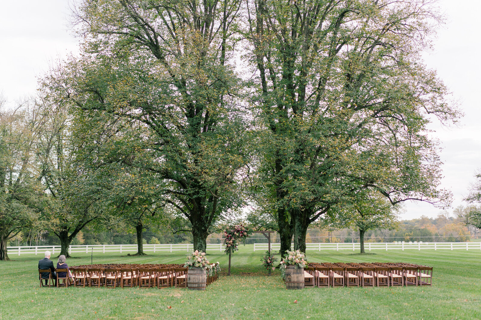 The ceremony site at Castle Hill Cider venue in Keswick, Virginia with two towering trees and a floral arch