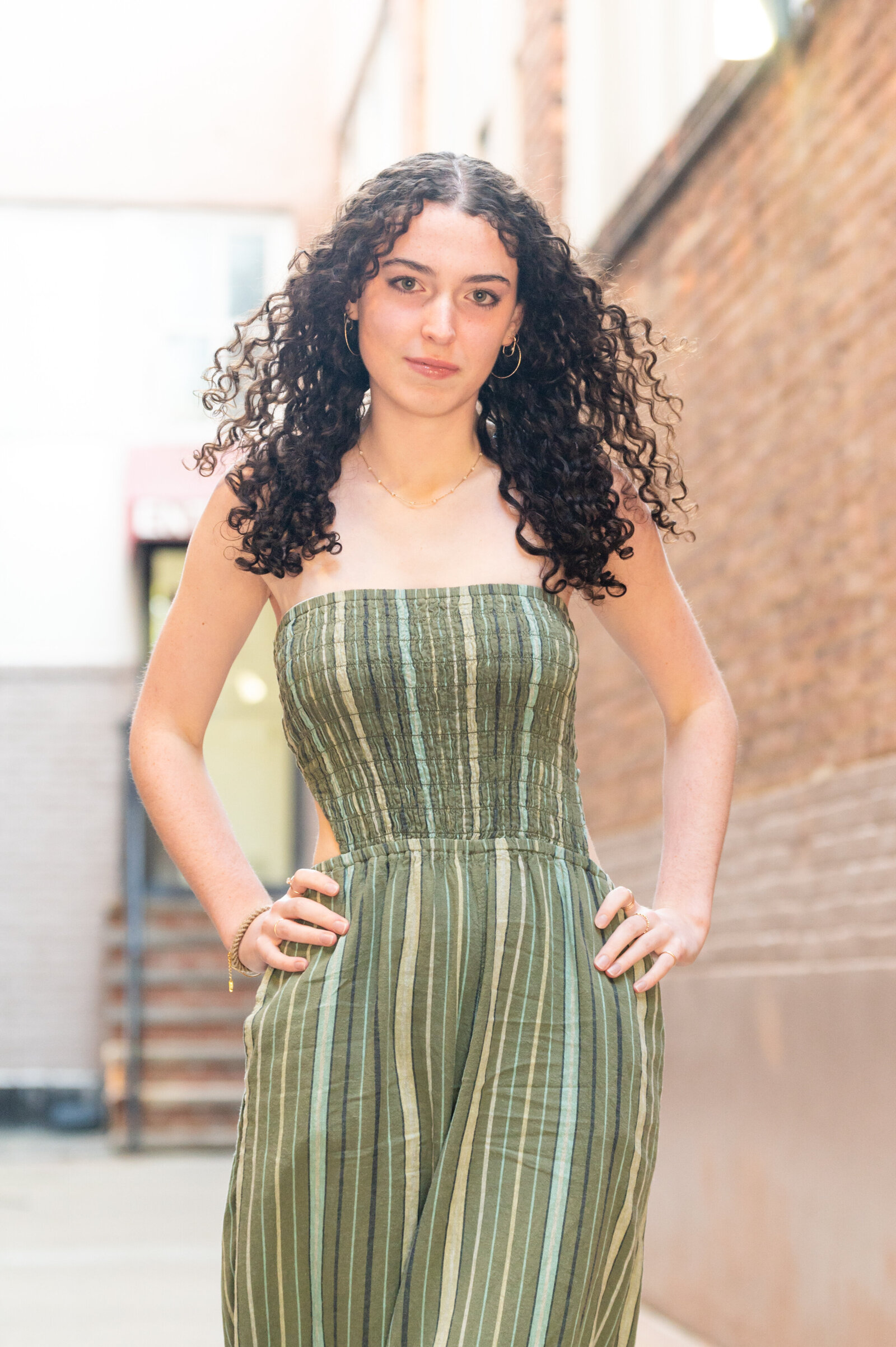 girl with curly hair, hands on hips and green striped romper senior portrait session