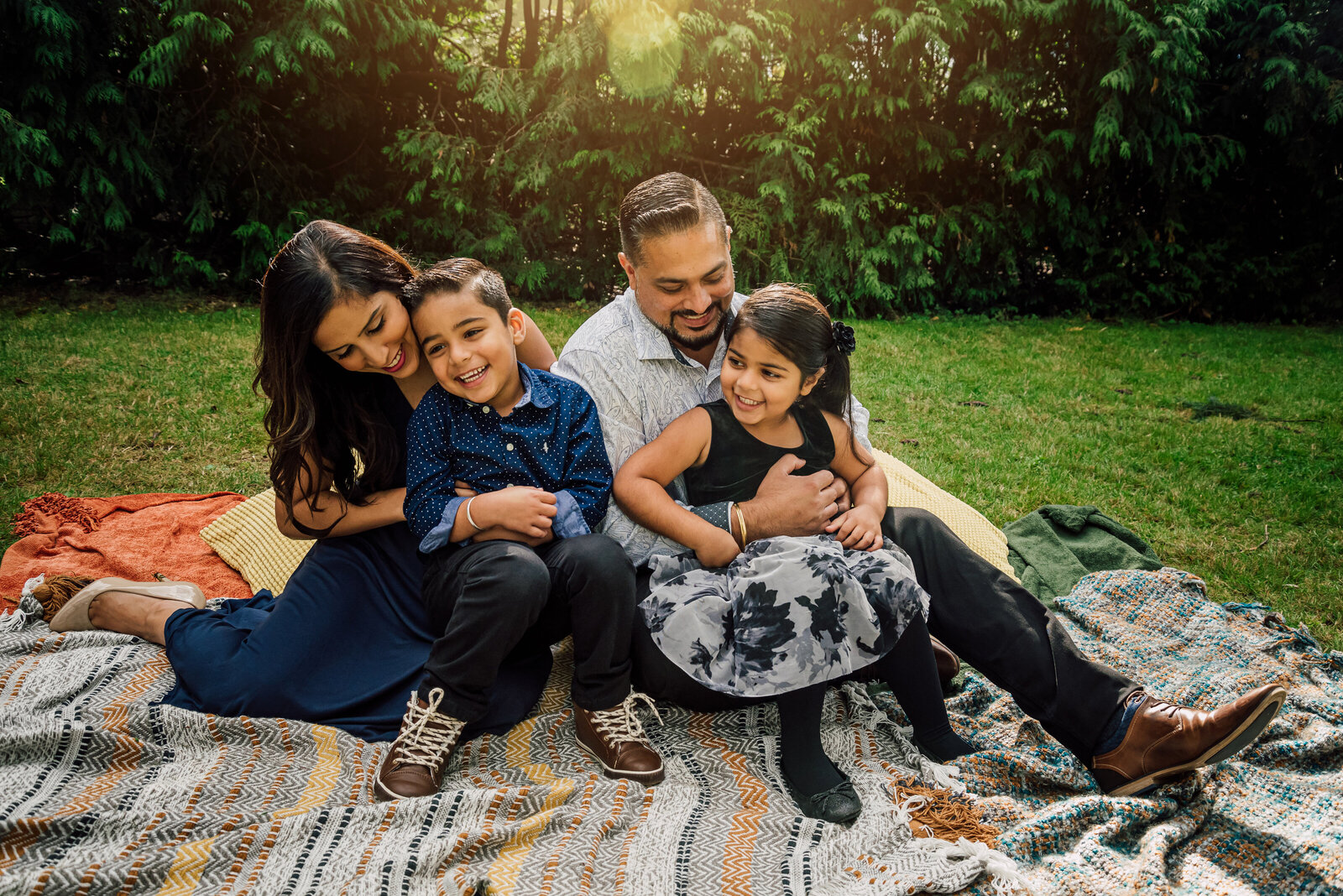 Family of four sitting on a blanket all lauging and smiling for the camera.