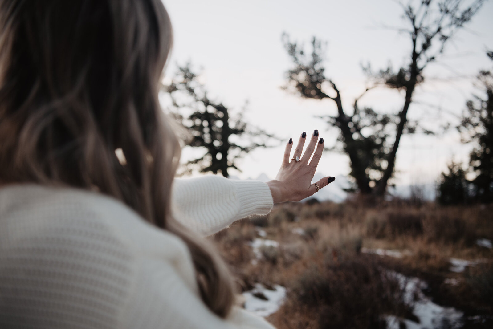 Grand Teton wedding winter pictures with bride holding out her hand and looking at her engagement ring photographed by jackson hole photographers