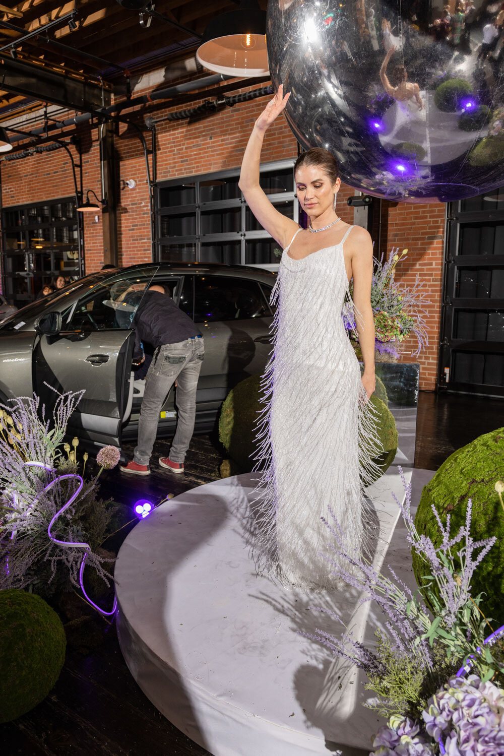 Woman in a fringe white gown posing under a disco ball near a car