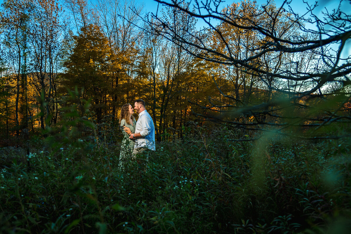 couple during engagement session in the woods during foliage at sunset