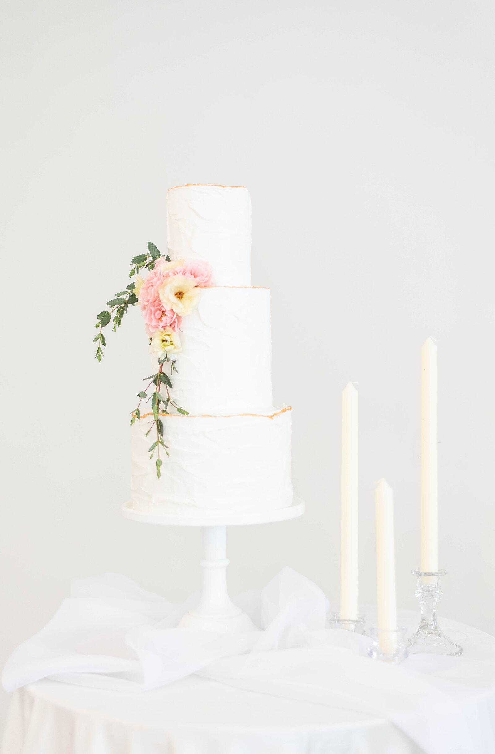 White wedding cake with pink flowers next to candlesticks