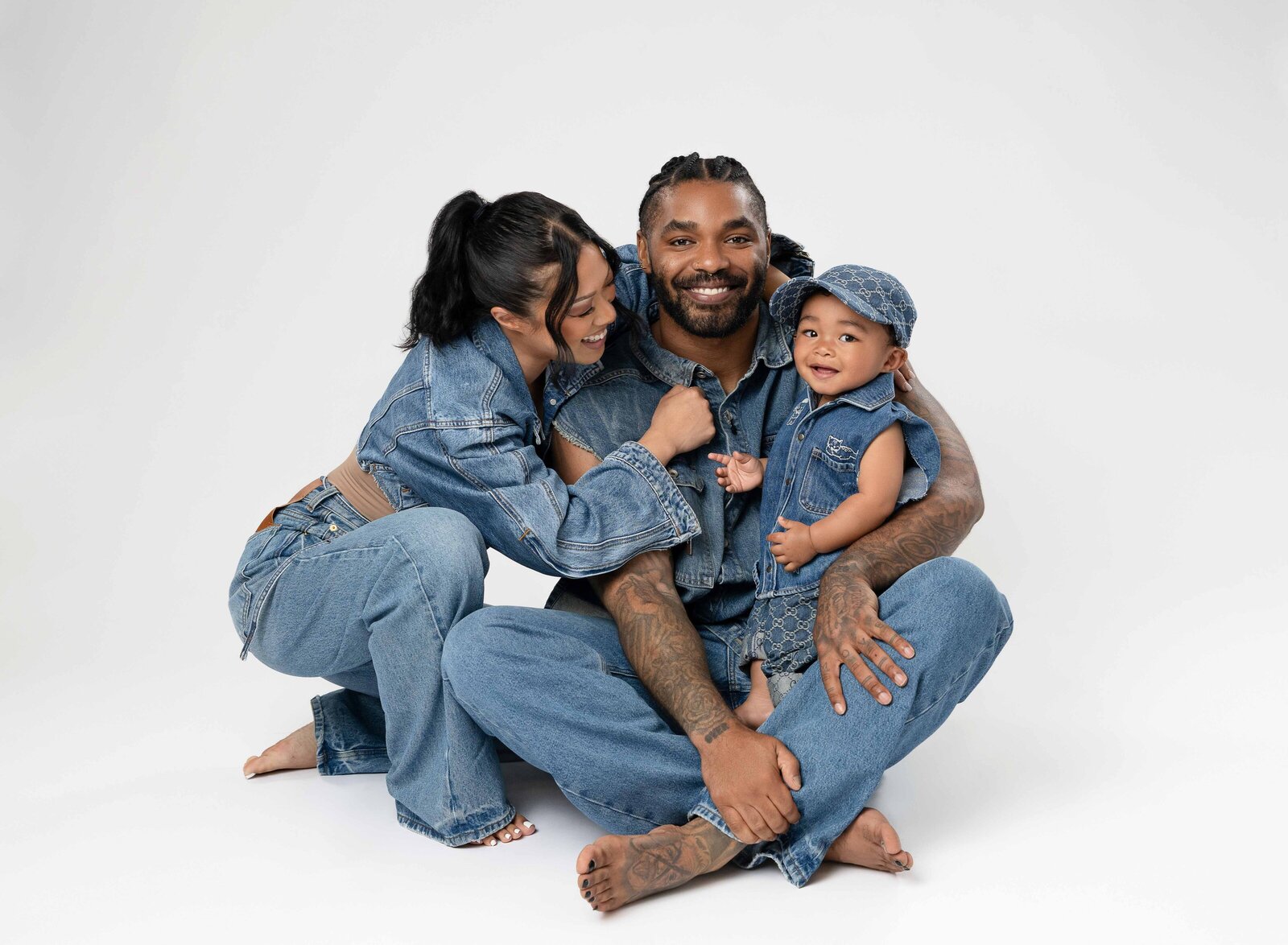 Dad sitting on floor with baby in his lap and Mom leaning in smiling at baby.