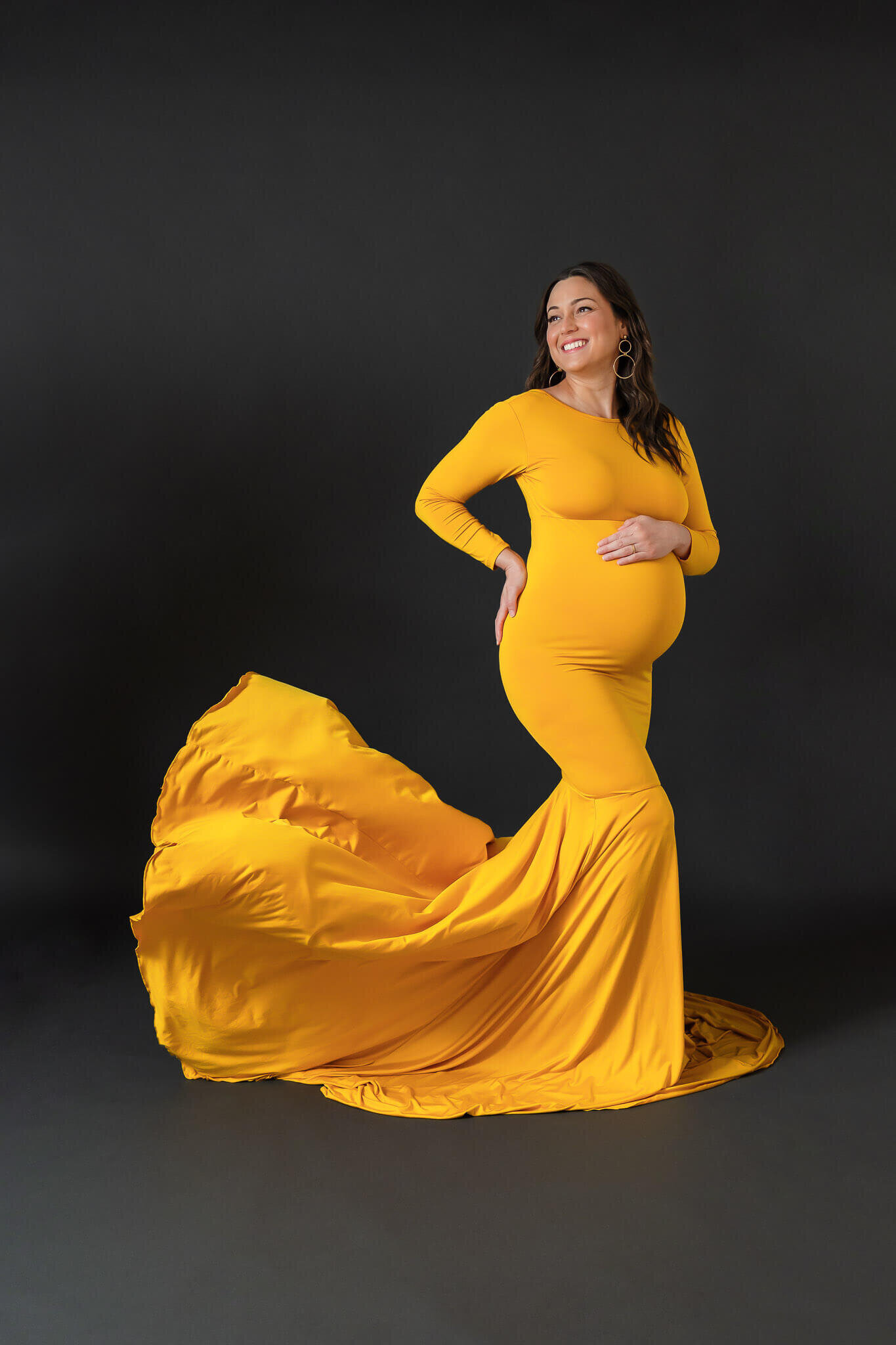 A mother-to-be in a yellow dress that has been tossed behind her.