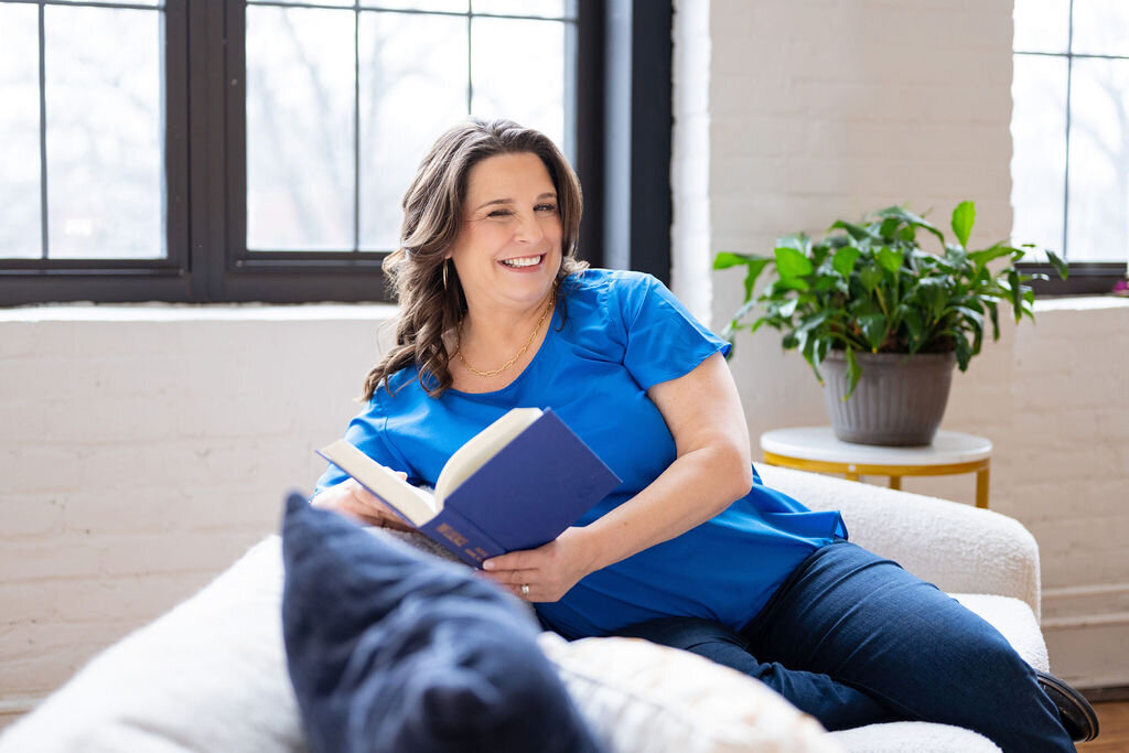 Dr. Chris Limone in a magenta blouse, smiling while holding a coffee mug during a virtual coaching session at her laptop