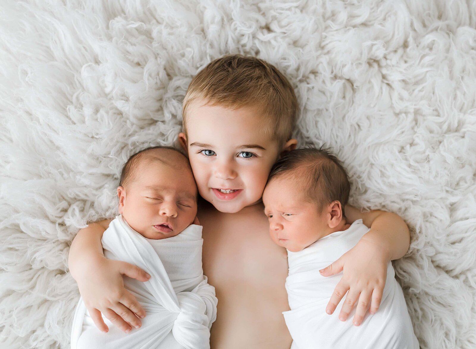 litlle boy holding his twin siblings
