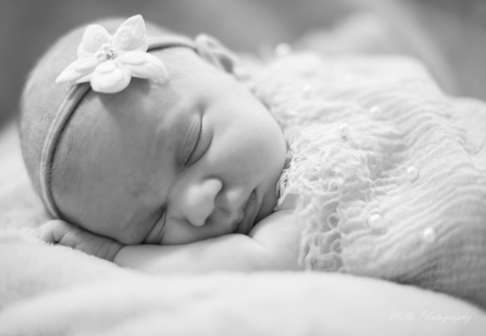 black and white phot of a newborn baby girl sleeping with a flower headband on her head photographed by Millz Photography in Greenville, SC