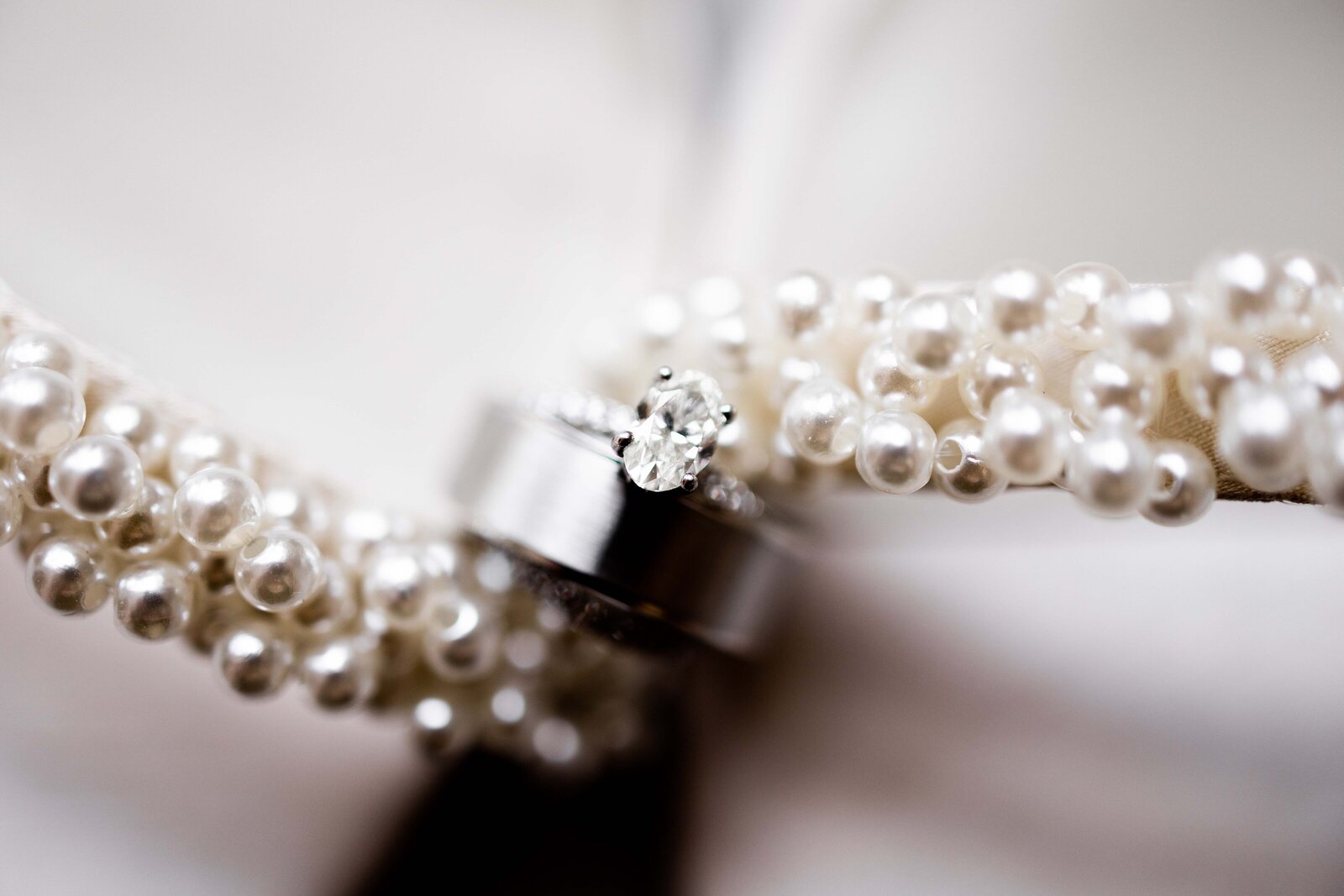 Dive into the exquisite details of wedding day elegance with this stunning image featuring a close-up of a sparkling engagement ring, sleek wedding bands, and pearl-covered bridal shoes. Perfectly arranged, this photograph captures the harmony and meticulous craftsmanship of each element, highlighting the thoughtful coordination that complements the bride's ensemble. Ideal for future brides and wedding planners seeking inspiration for luxurious and detailed accessory choices that add a touch of sophistication to any wedding theme.