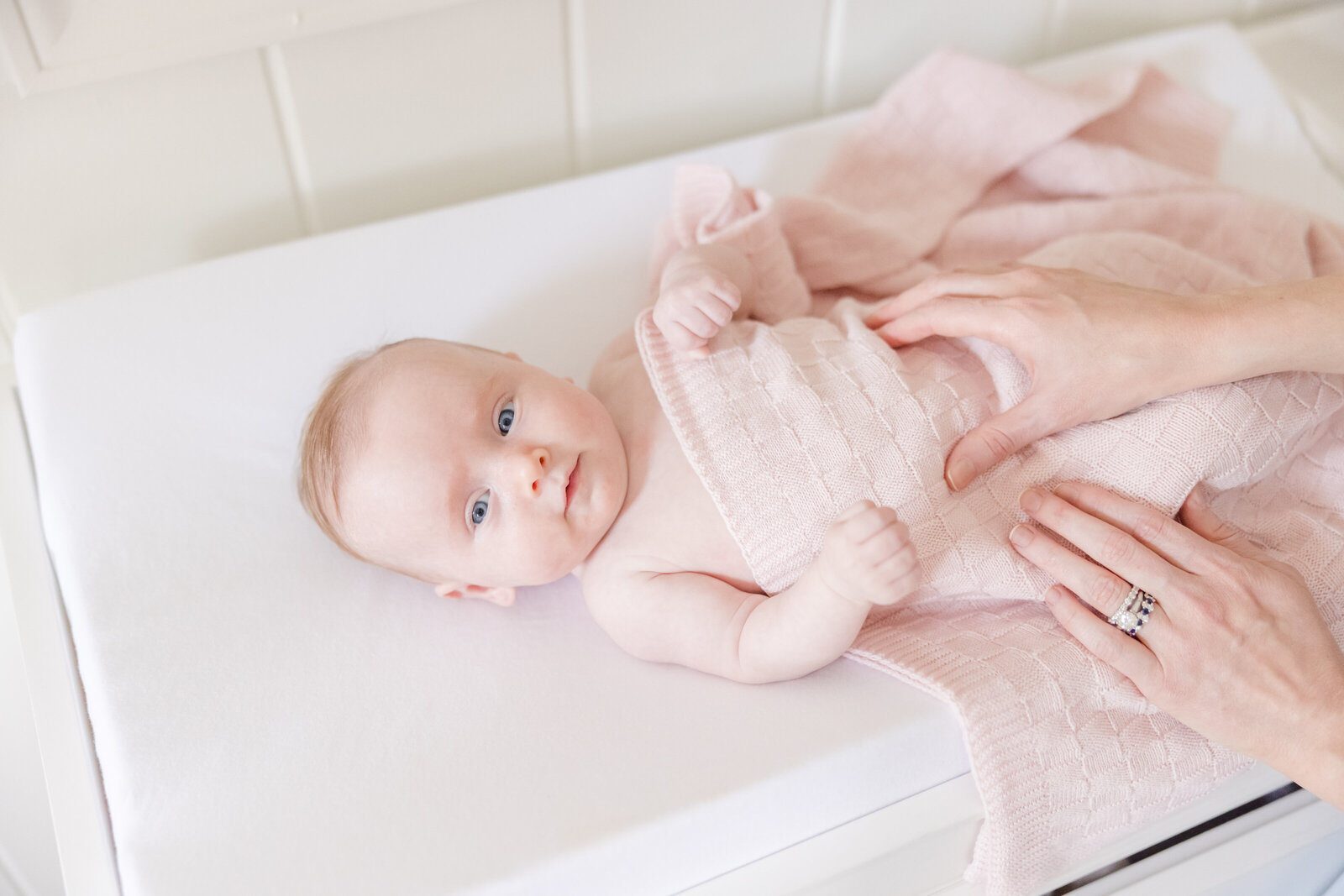 Baby laying on a changing table covered by a pink blanket.