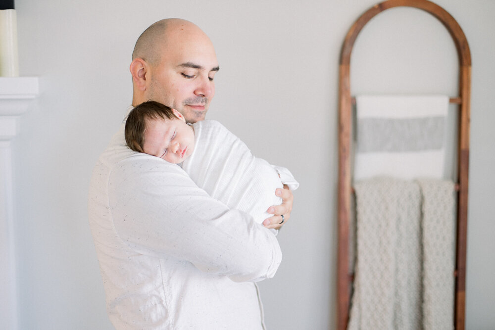 Image of new father holding newborn baby wrapped in white blankets taken by Newborn Photographer Sacramento Kelsey Krall