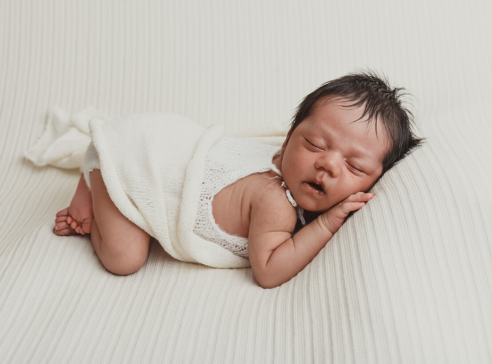 newborn baby laying on stomach with white blanket