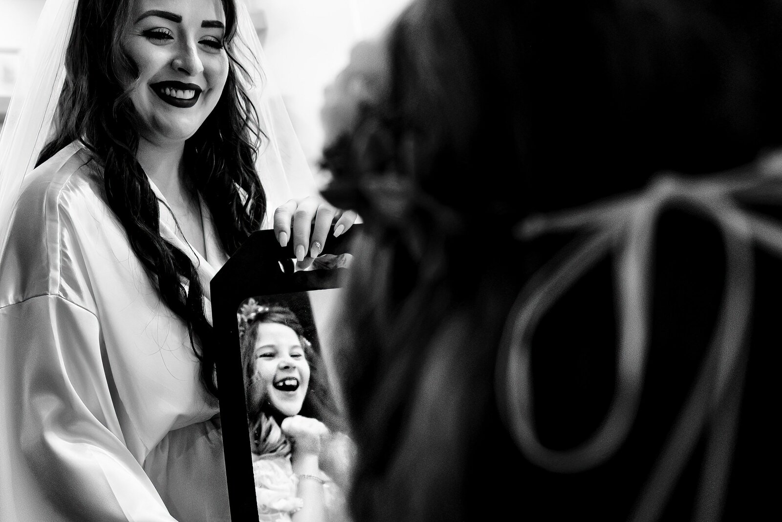 bride holds up a mirror for the flower girl to see herself; flower girls expression in the mirror is excited