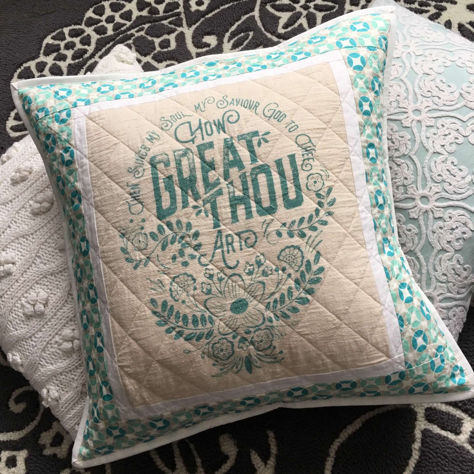 Quilted pillow with How Great Thou Art print in center.