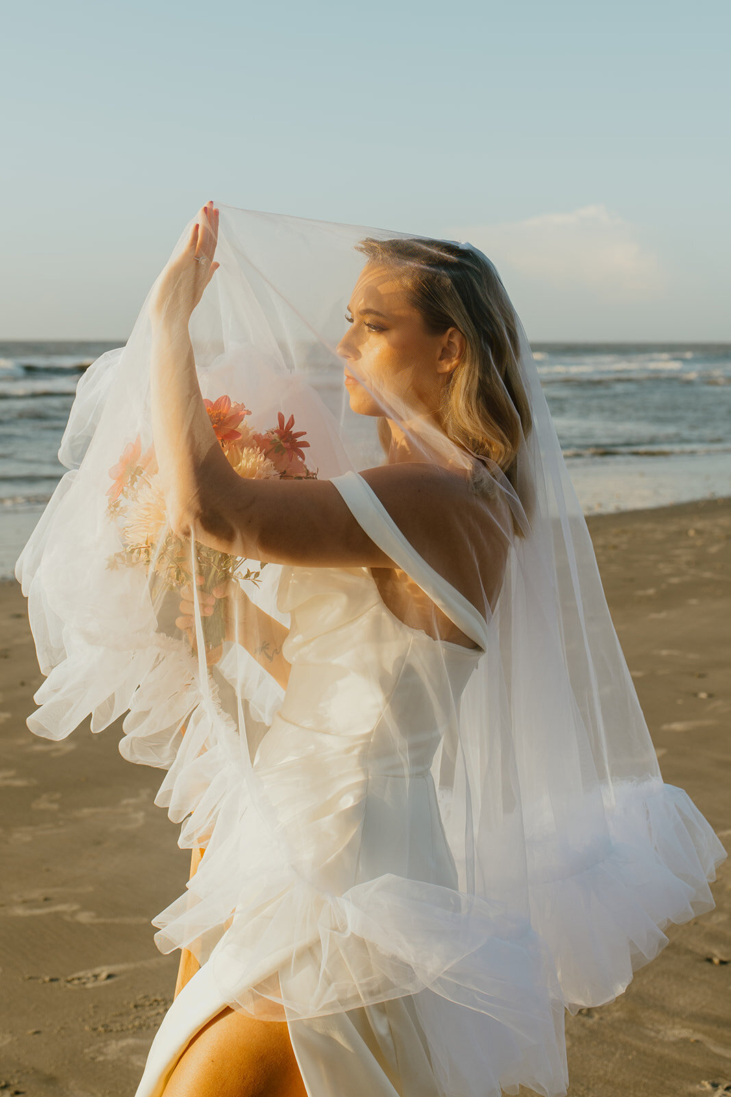 bride faces sun at beach while under veil
