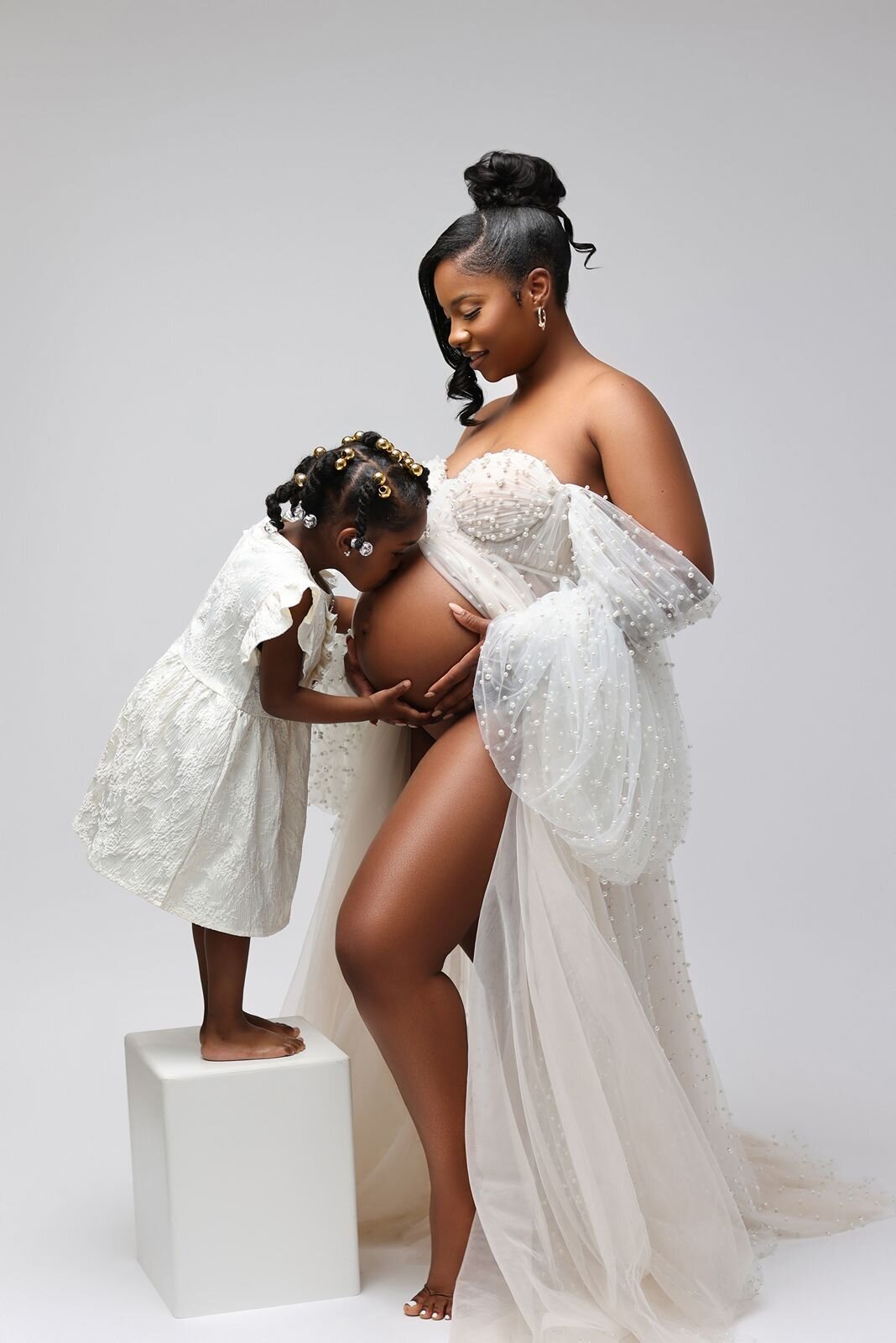 Heartwarming scene of a mother in a white outfit with her child kissing her belly