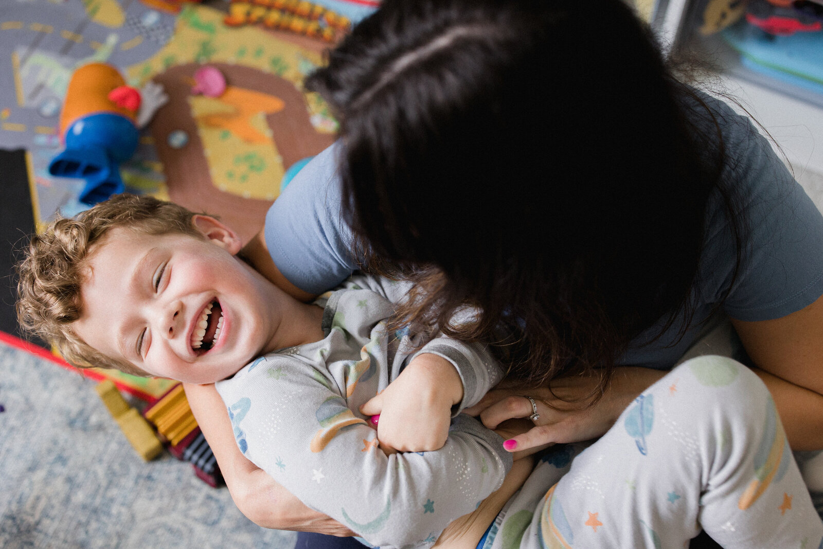 Mom tickles little boys belly while she looks down at him laughing