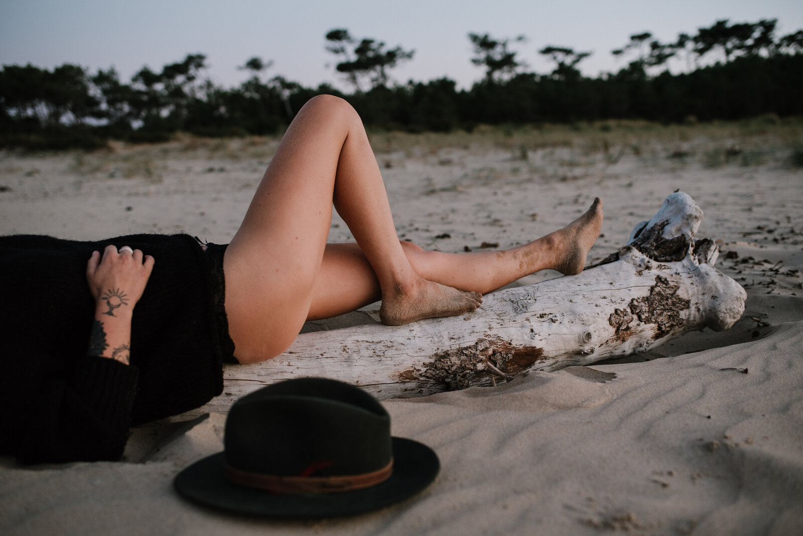 woman laying on a trea woman laying on dead tree, on a beach, her feet are bare and covered in sand