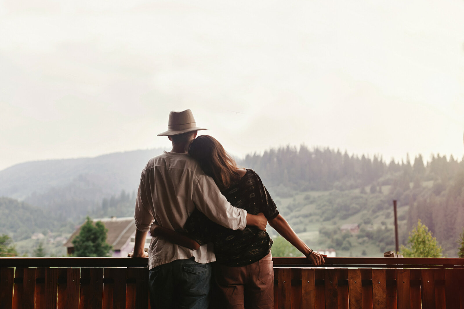 hipster-couple-hugging-on-porch-of-wooden-house-lo-2AJWSYH