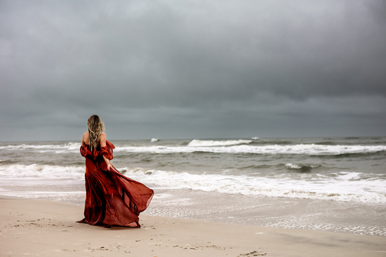Pregnant woman walking away from camera, towards the ocean