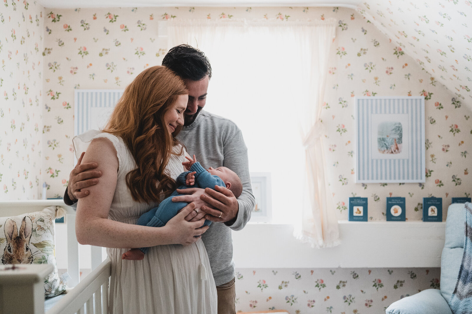 Parents standing close together, lovingly gazing at their sleeping newborn wrapped in blue knitwear