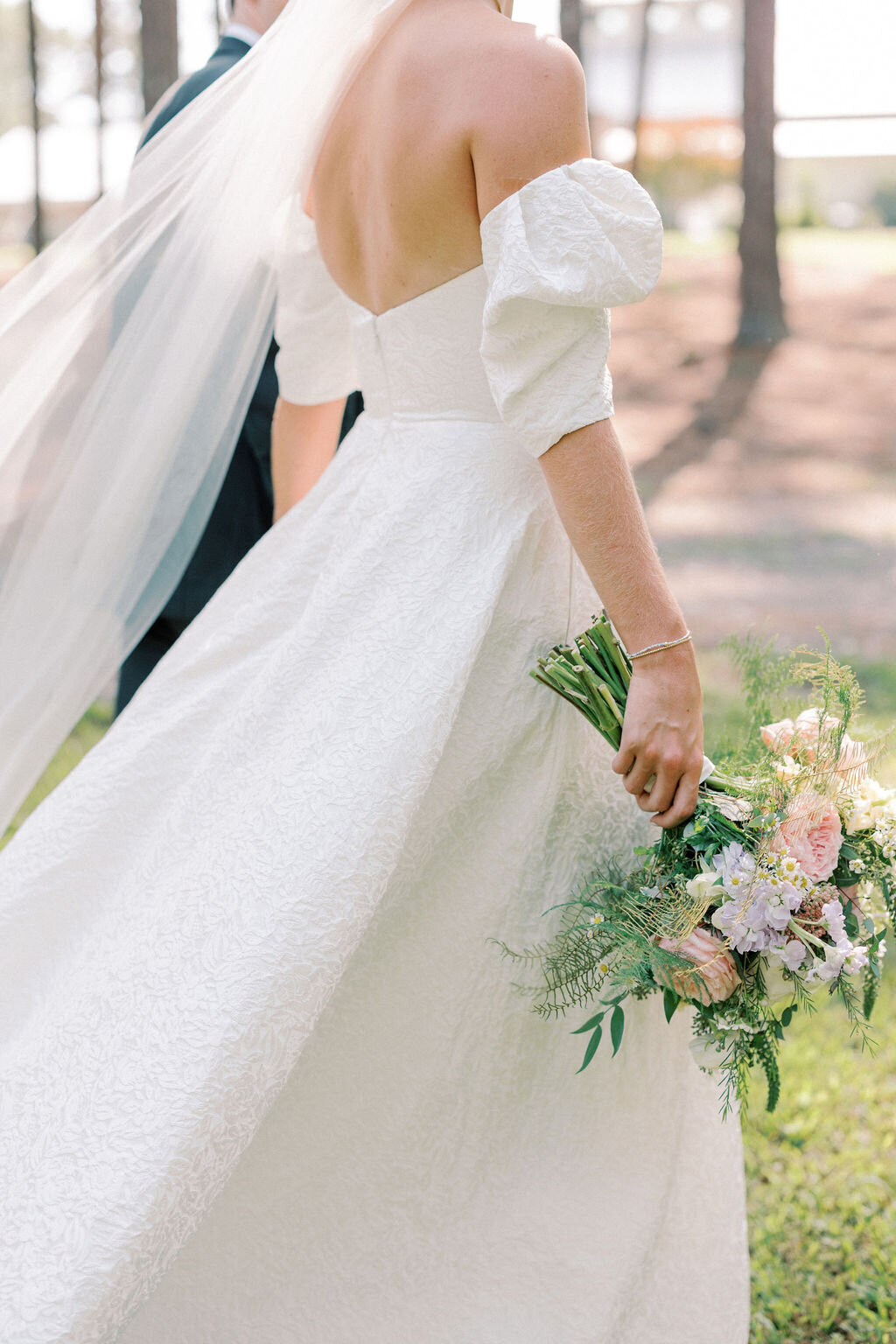 Bride in long white dress holds bouquet of pink flowers in motion