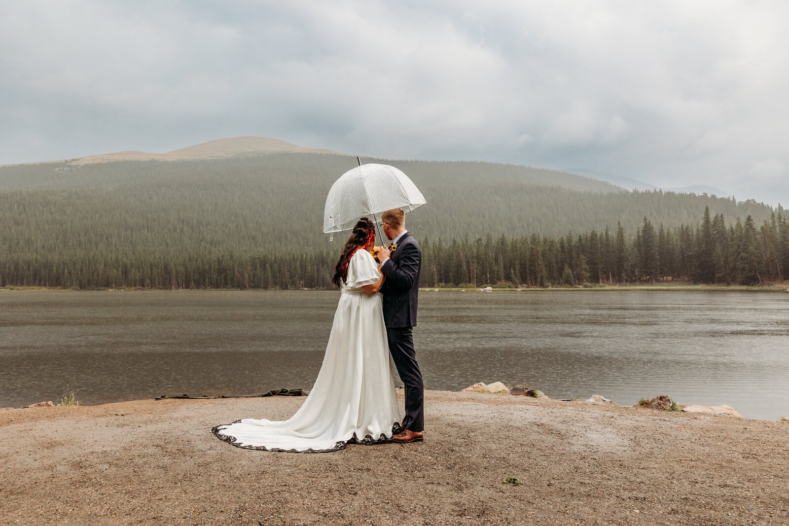 Wedding Photographer in Boulder Colorado captures bride and groom standing under clear umbrella after elopement