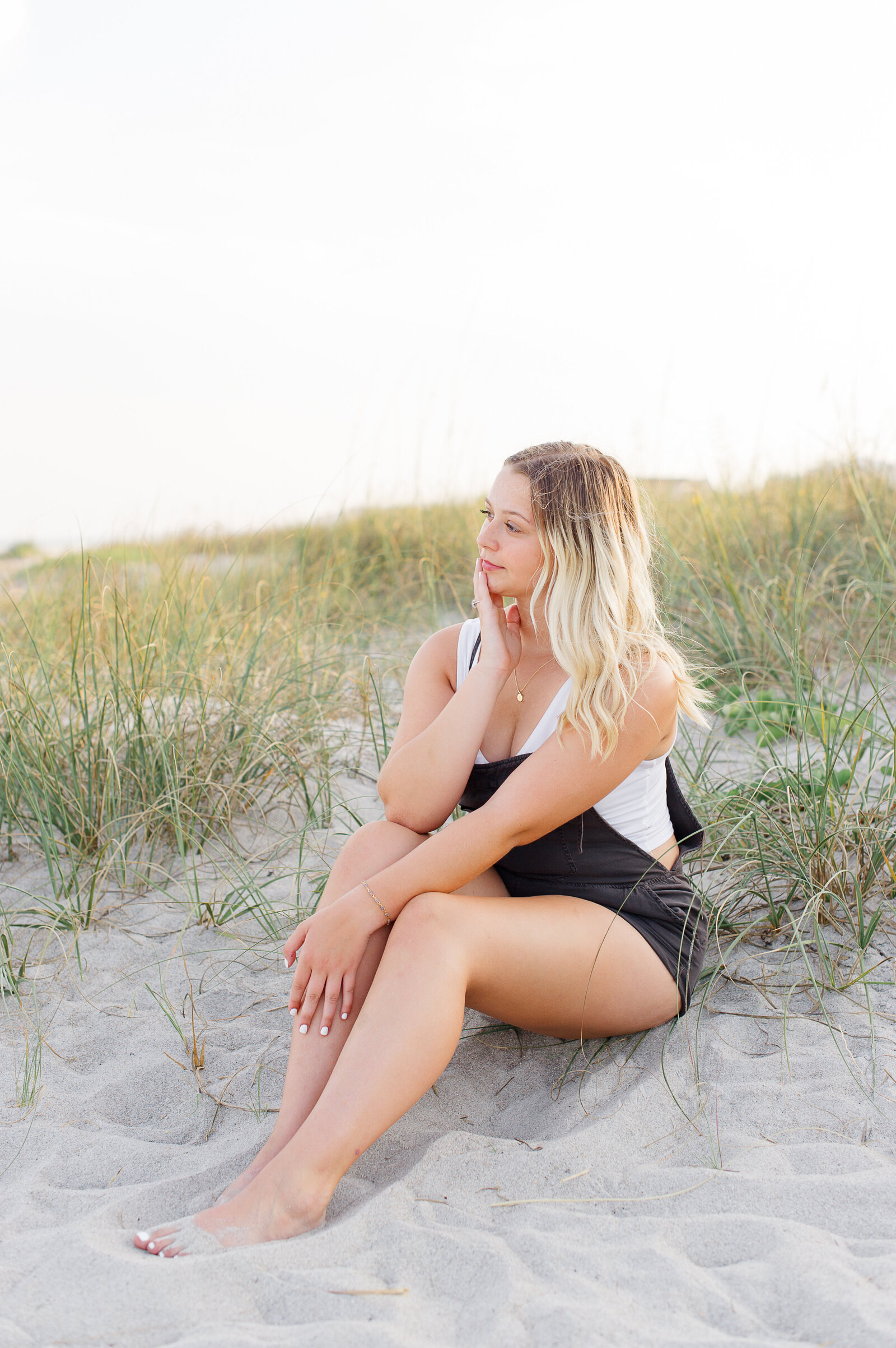 Young girl sitting in the dunes at sunset watching the waves crash on the beach