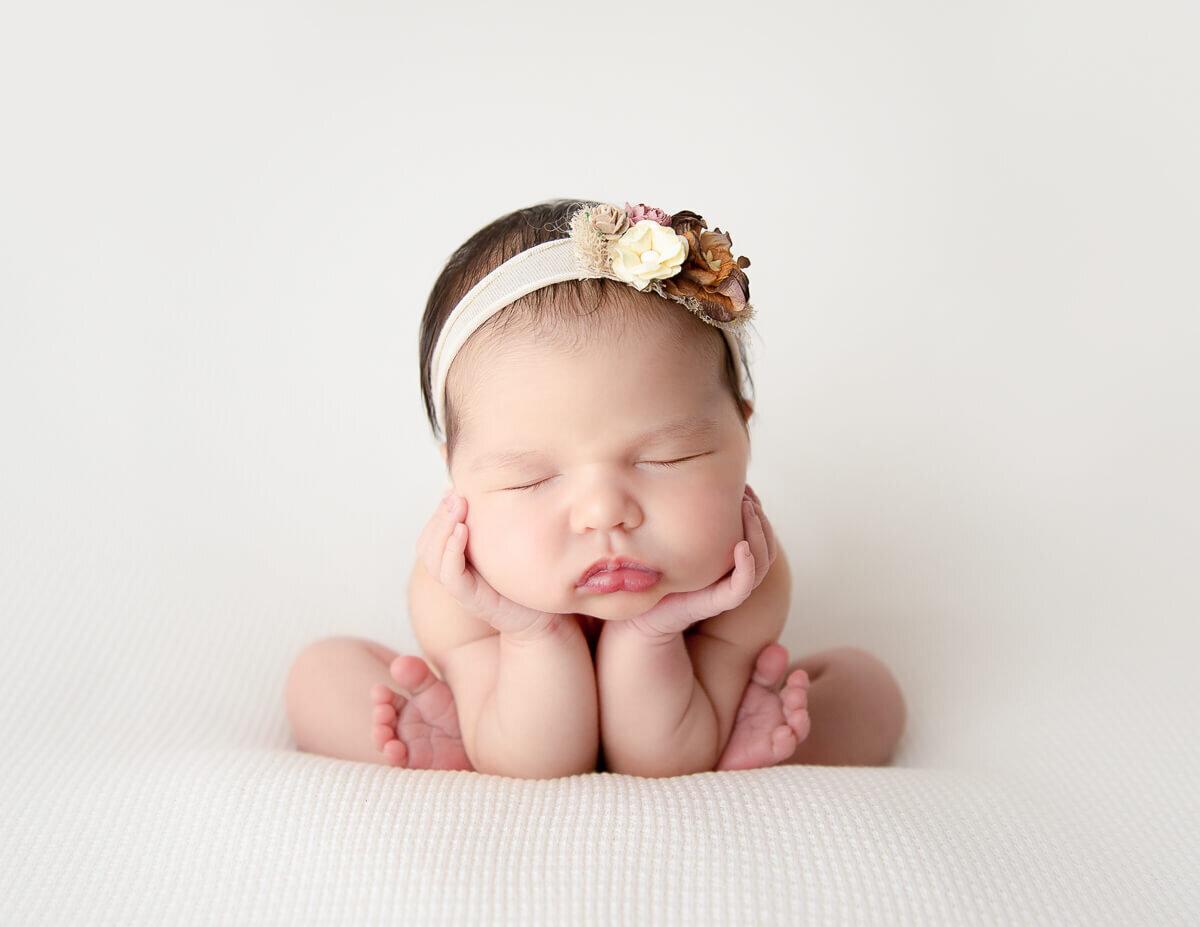 Newborn girl peacefully posed in frog position amidst a soft backdrop at a photography studio in Rochester, NY, showcasing her innocence and delicate features.