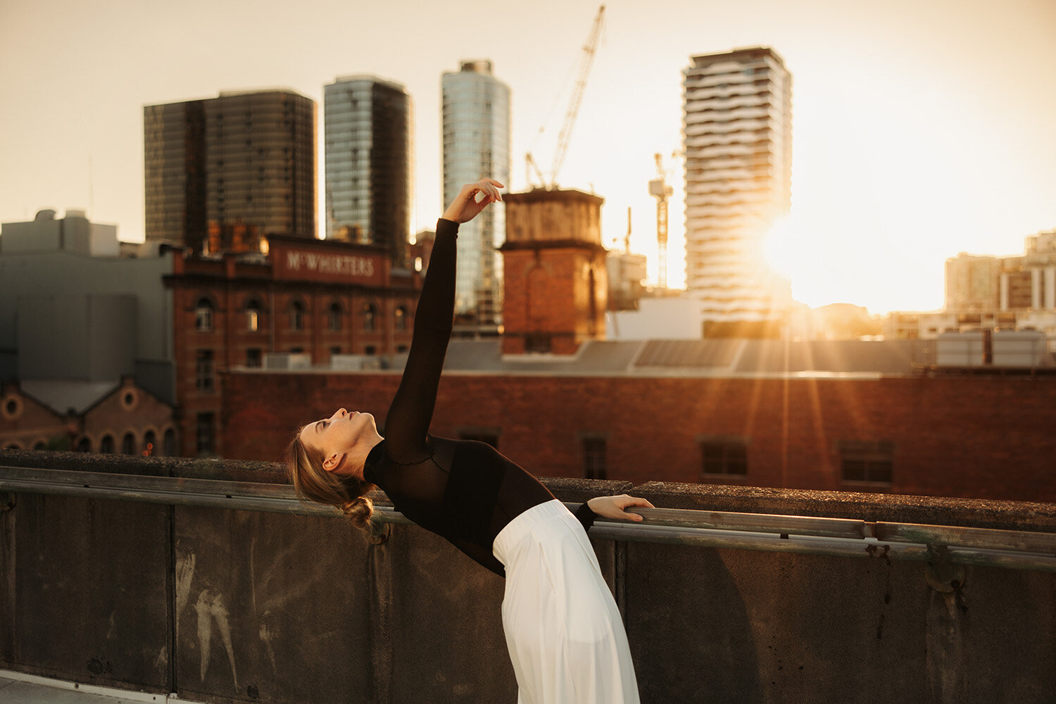 Dynamic brand photography featuring a woman stretching joyfully against a city skyline at golden hour.