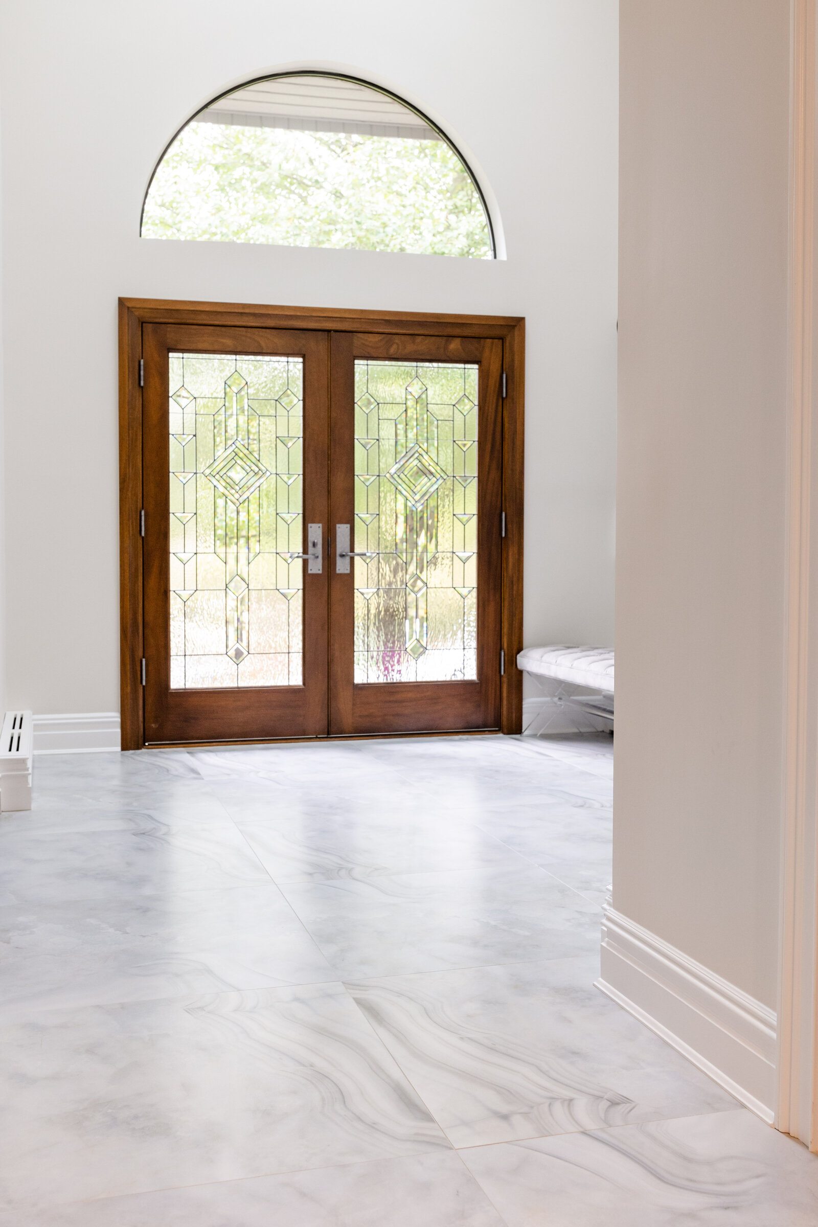 The entryway is designed with high ceilings, an arch window, double doors, and large-format porcelain tiles.