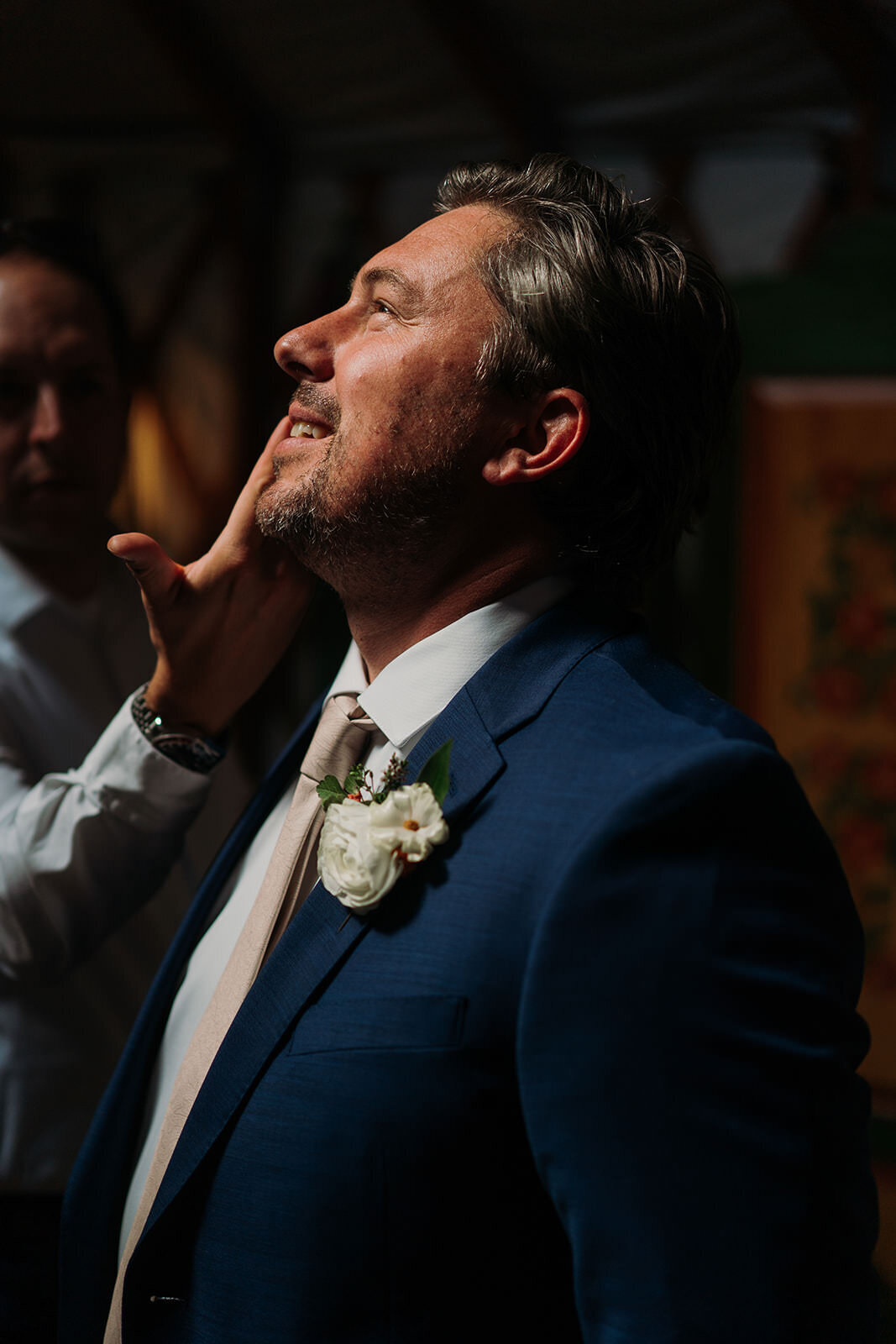 A groom looking up and smiling as someone touches their face.