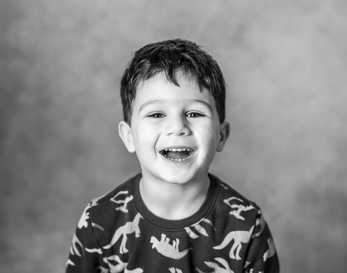 A young child smirks in a dino shirt.