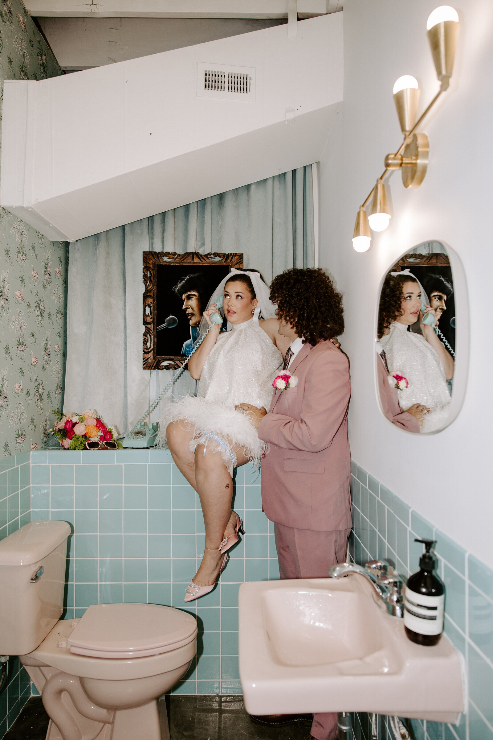 A couple pretends to pick up the phone at a wedding chapel in a bathroom.