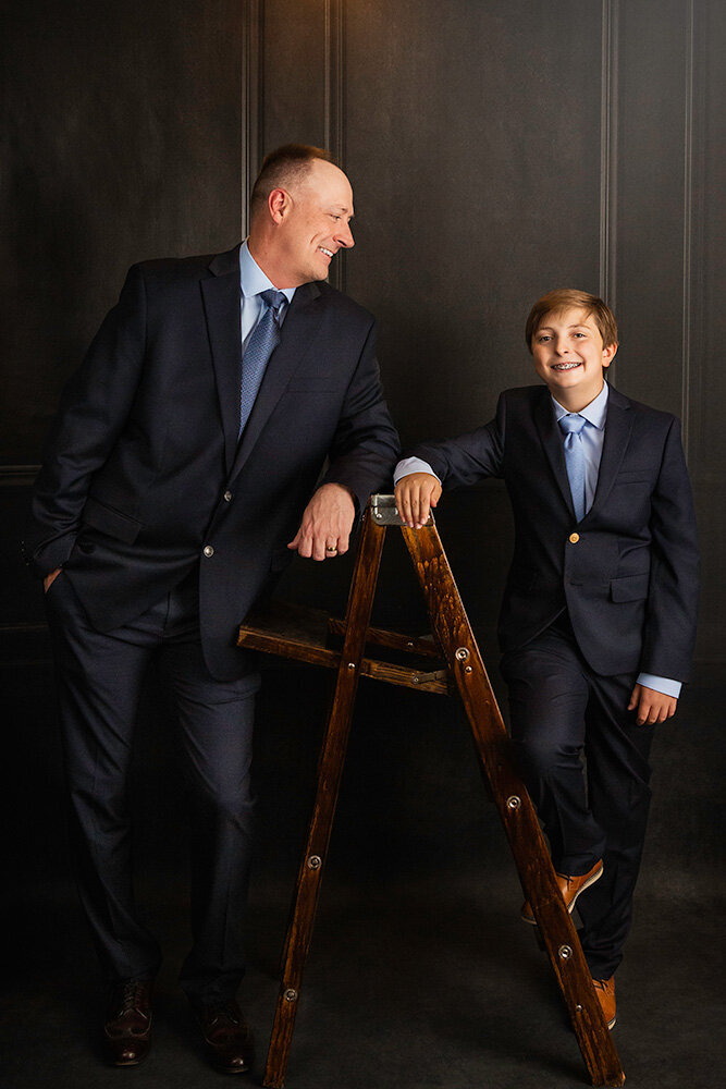 candid-father-son-vanity-fair-blue-suits-handsome-father-like-son-ladder-dark-studio-background-regal-upscale