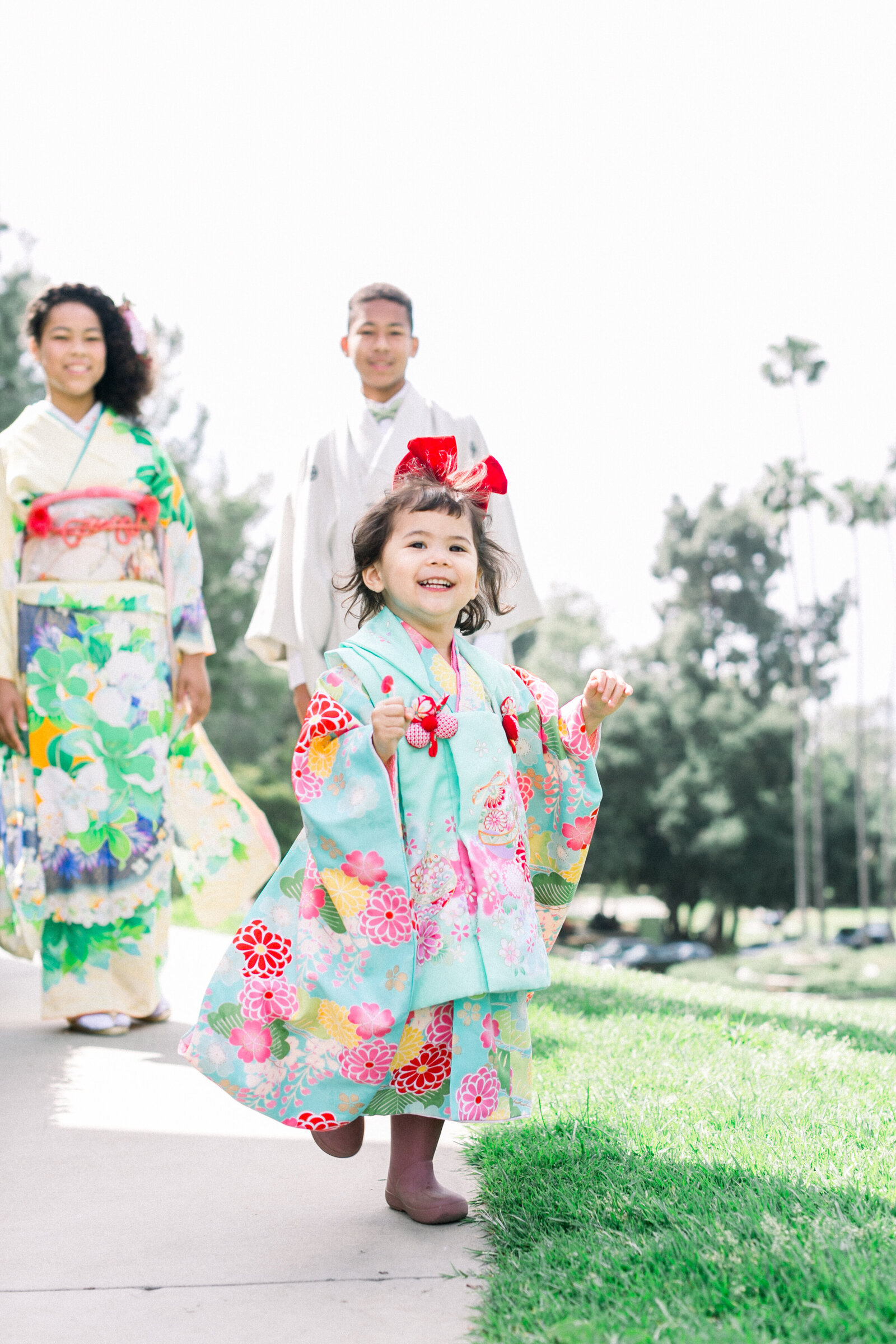 Smiling girl in turquoise kimono running with family and palm trees in background | 七五三 家族と女の子 着物 パームツリー ロサンゼルス