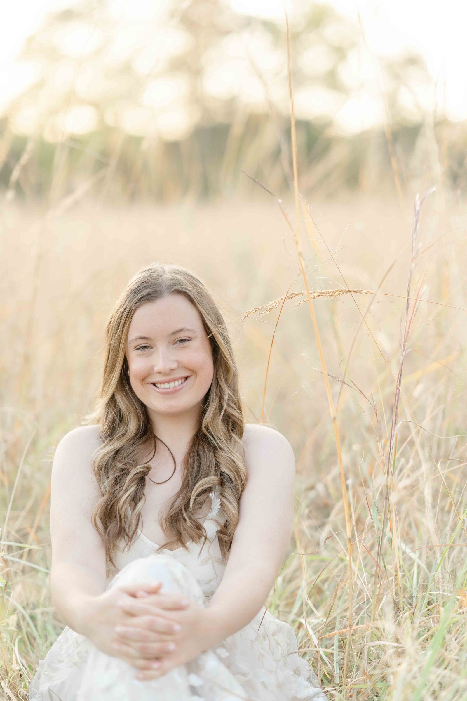 girl sitting on the middle of a field smiling during Ashburn, Virginia senior picture