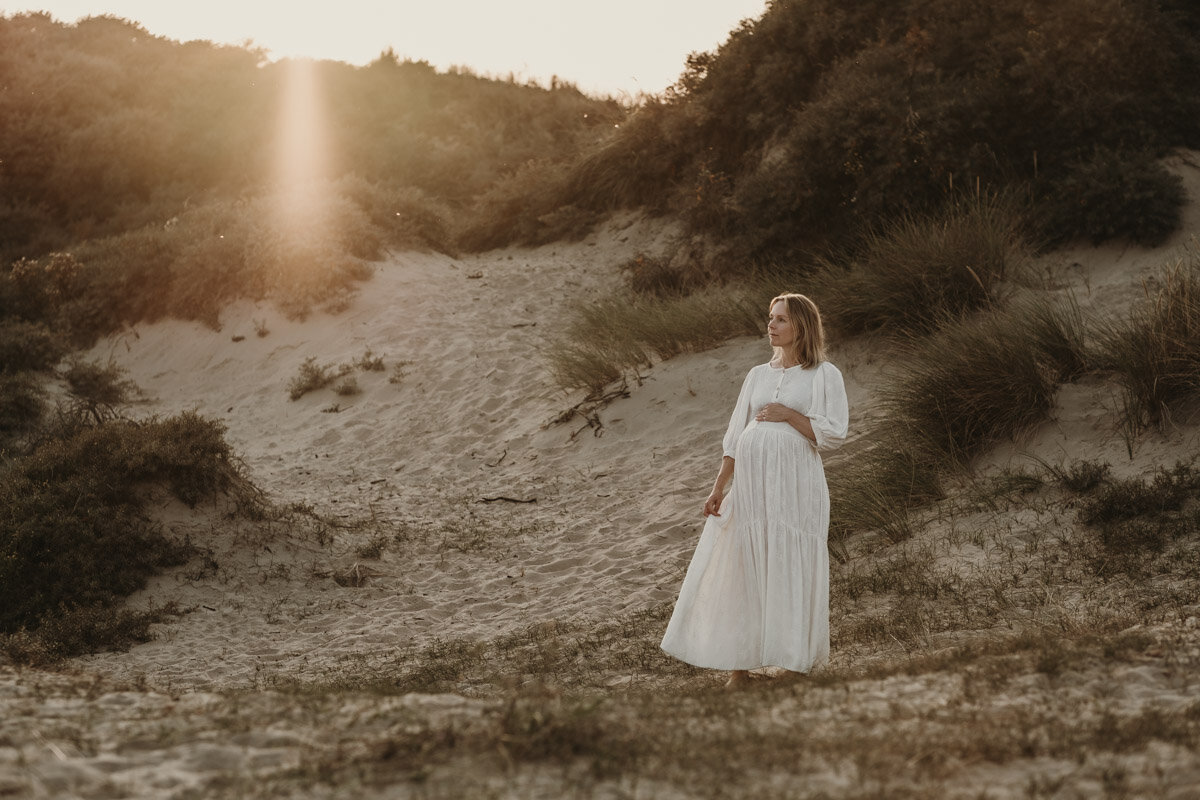 zwangere vrouw in de duinen tijdens zonsondergang