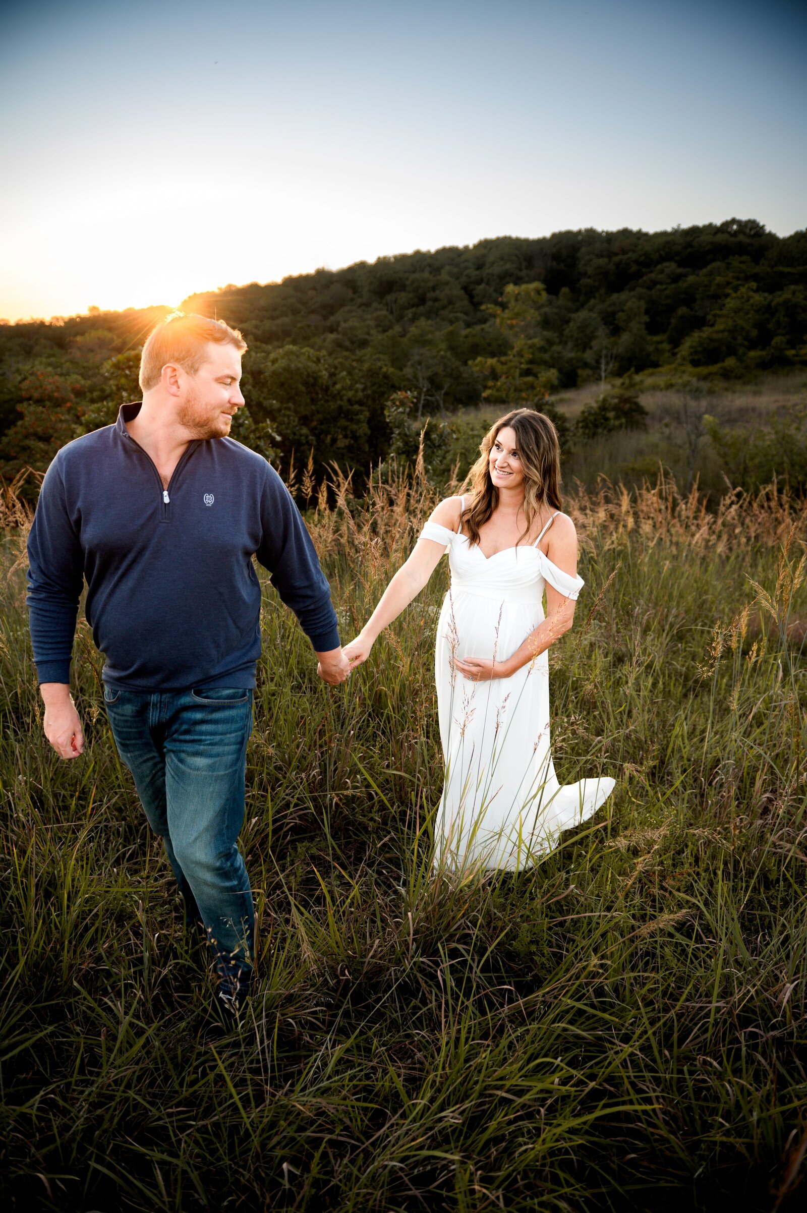 husband holding pregnant wife hand as the walk through a field