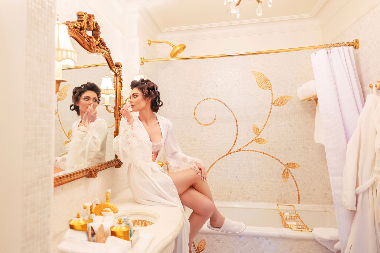 Bride in bathrobe sitting on bathroom counter looking in mirror