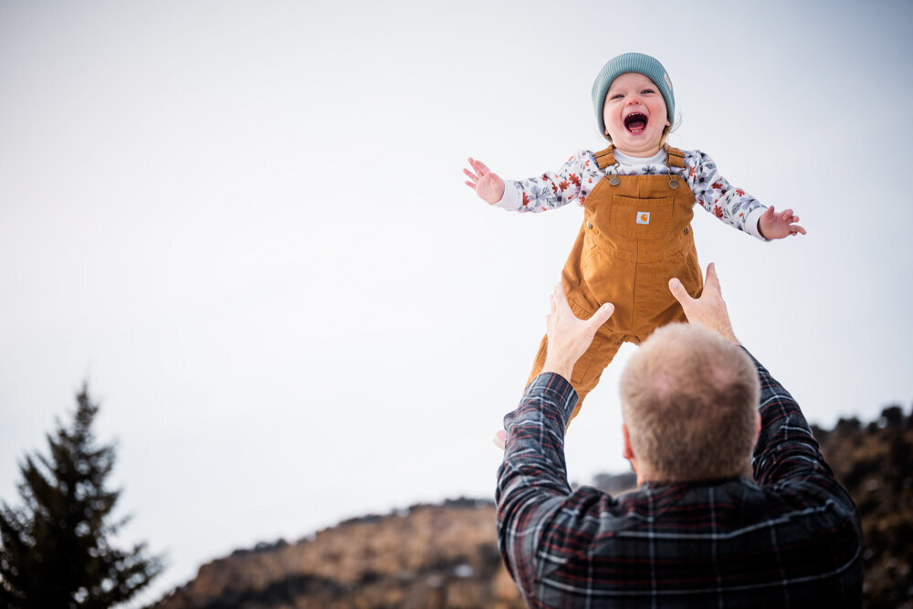 a dad throws his daughter into the air and she giggles