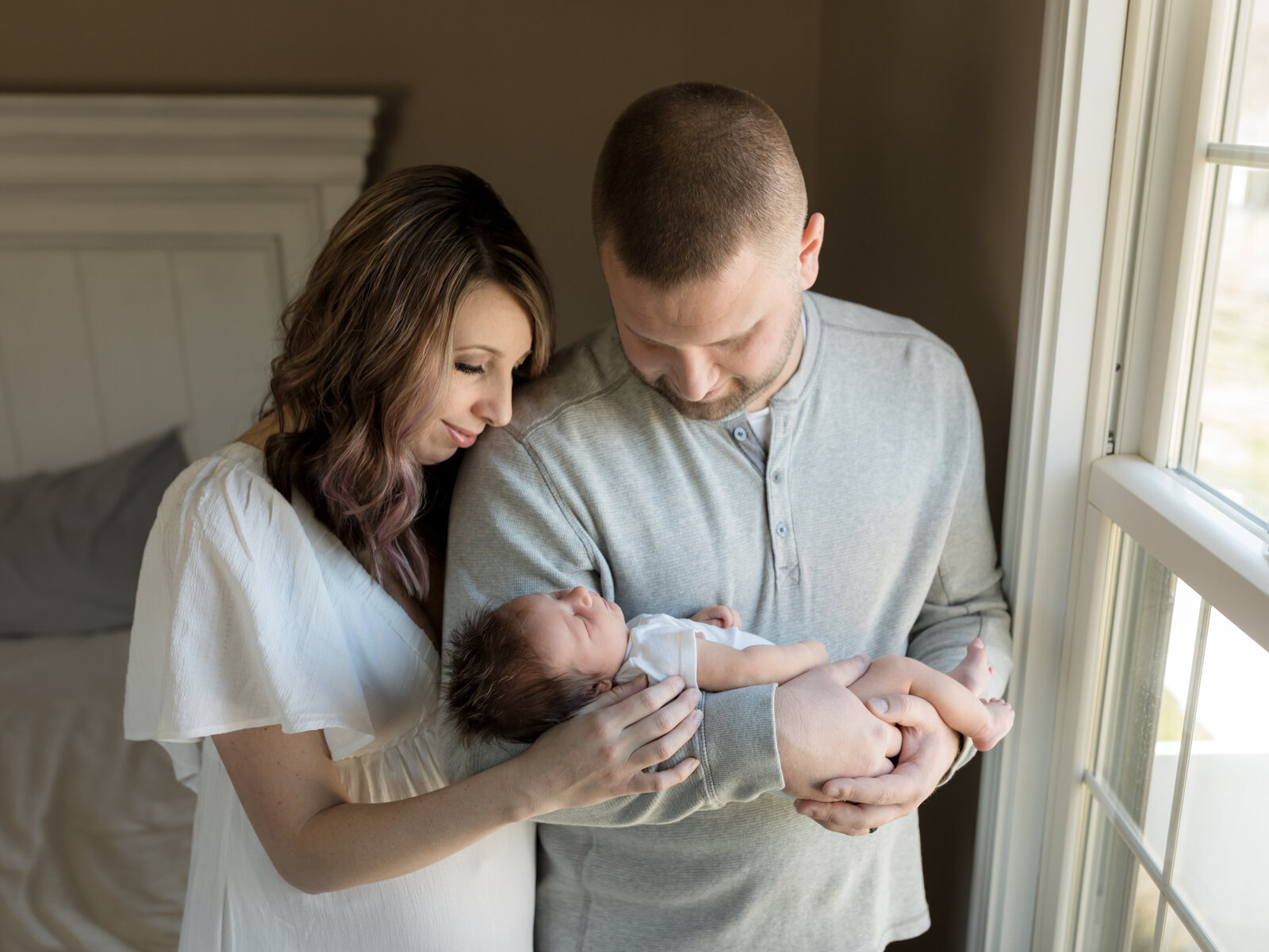 mom and dad holding newborn baby boy by window for in home lifestyle session