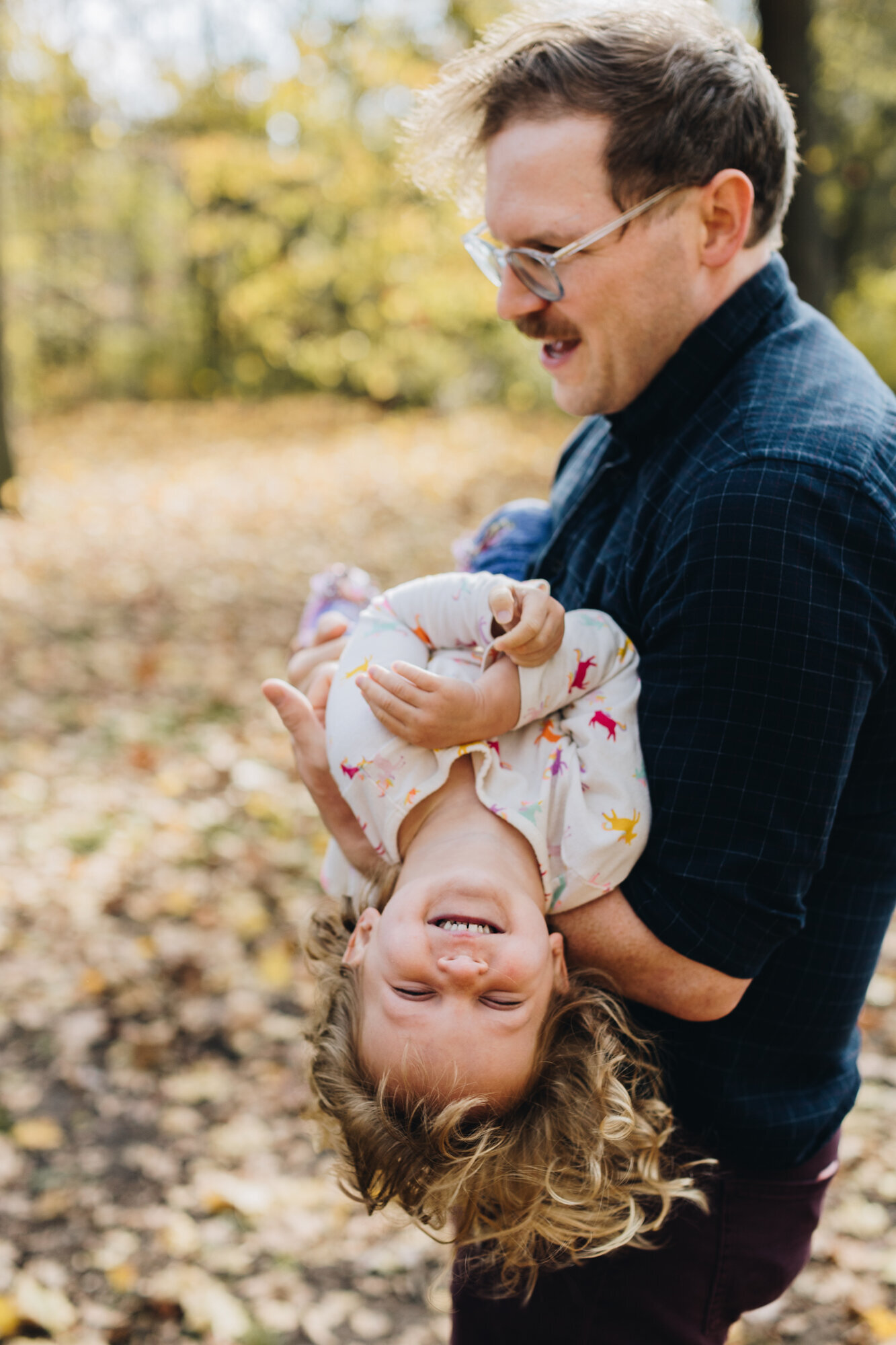Dad playfully holding his laughing toddler upside down during a Hudson Valley family photography session