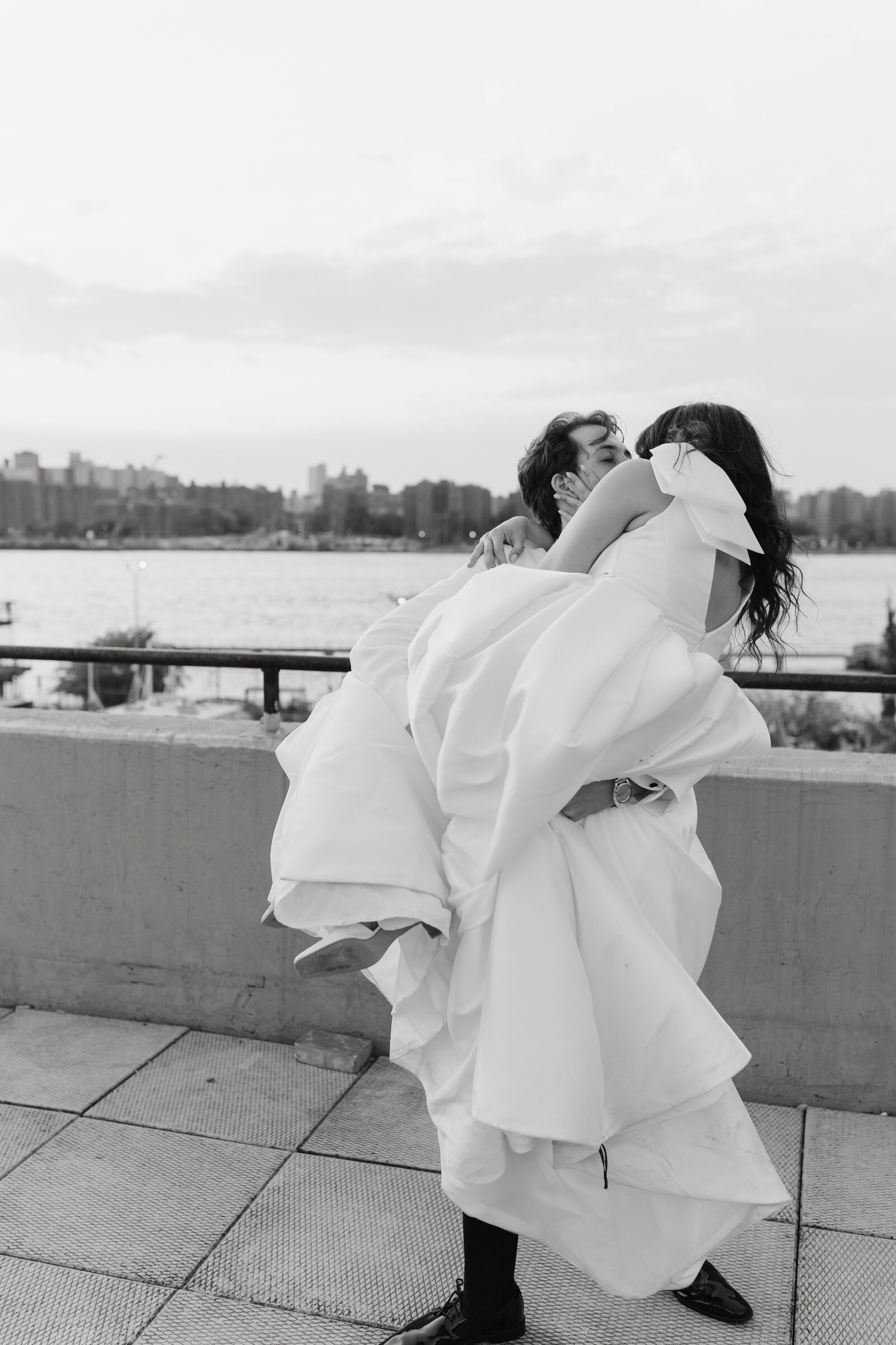 Black and white image of groom holding bride in romantic way while kissing her in front of the NY city skyline | Emma LeeAnn Photography