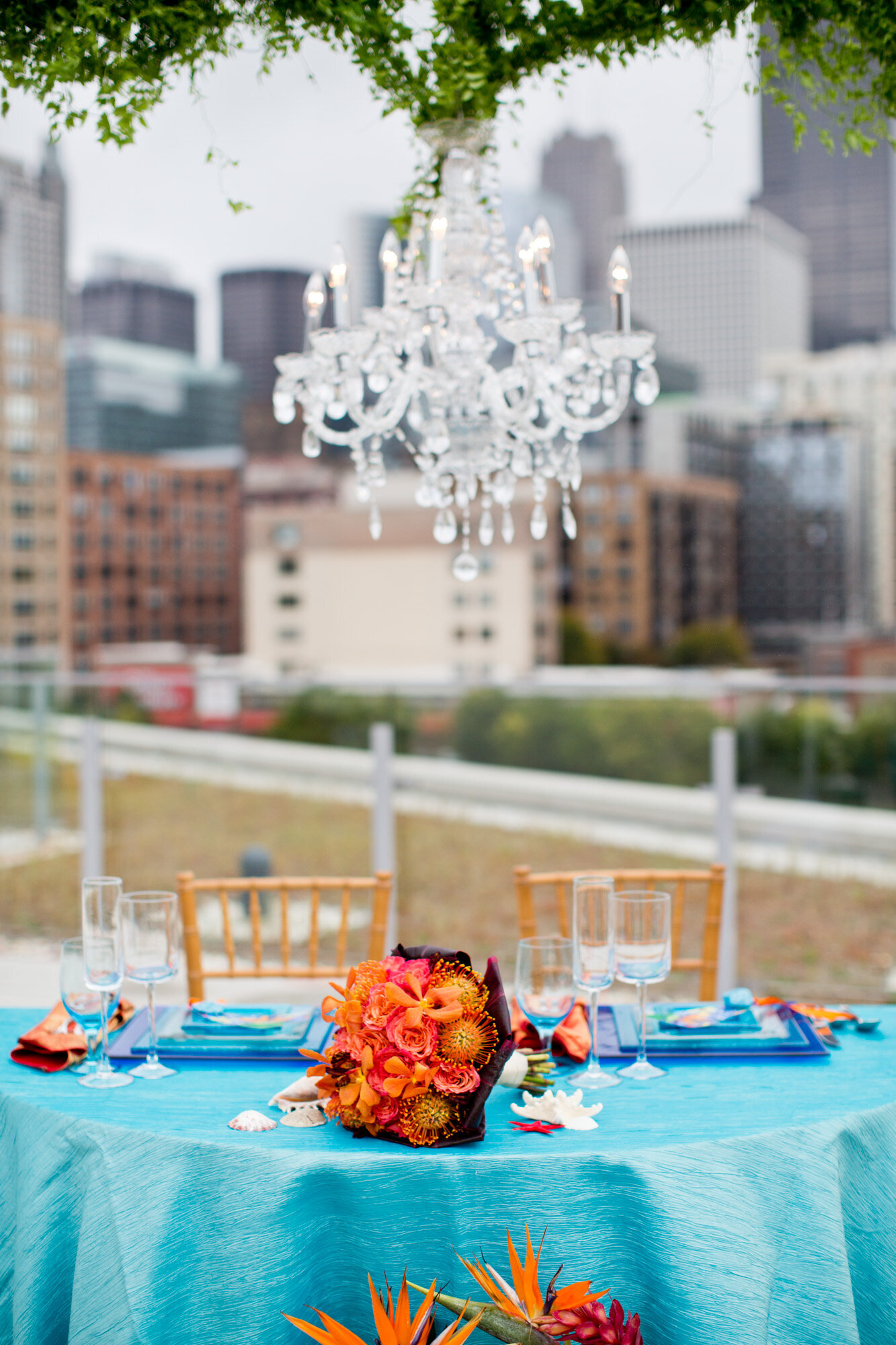 Wedding reception round table for newly married couple with blue cloth, golden chairs, floral centerpiece and chandelier on top