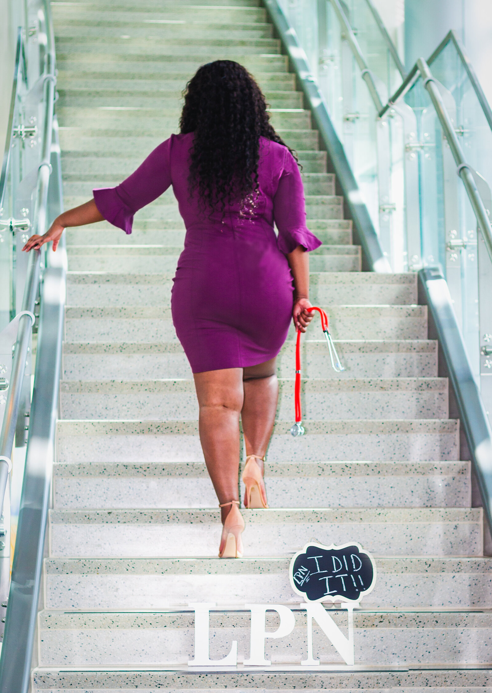 girl in purple dress walking up stairs hold stethoscope. The letters LPN and sign are the stairs.