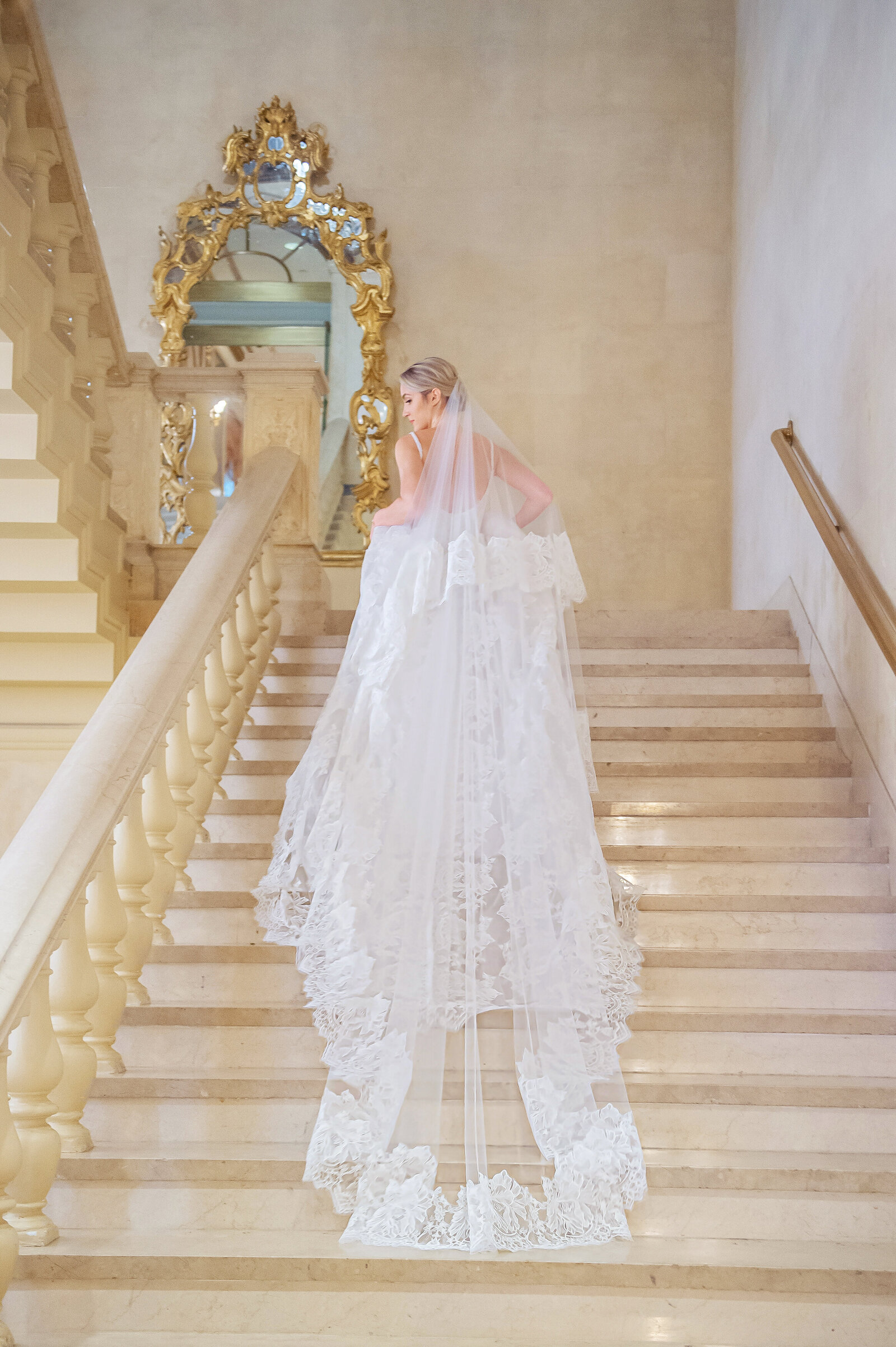 Bride with log veil walking up marble stairs