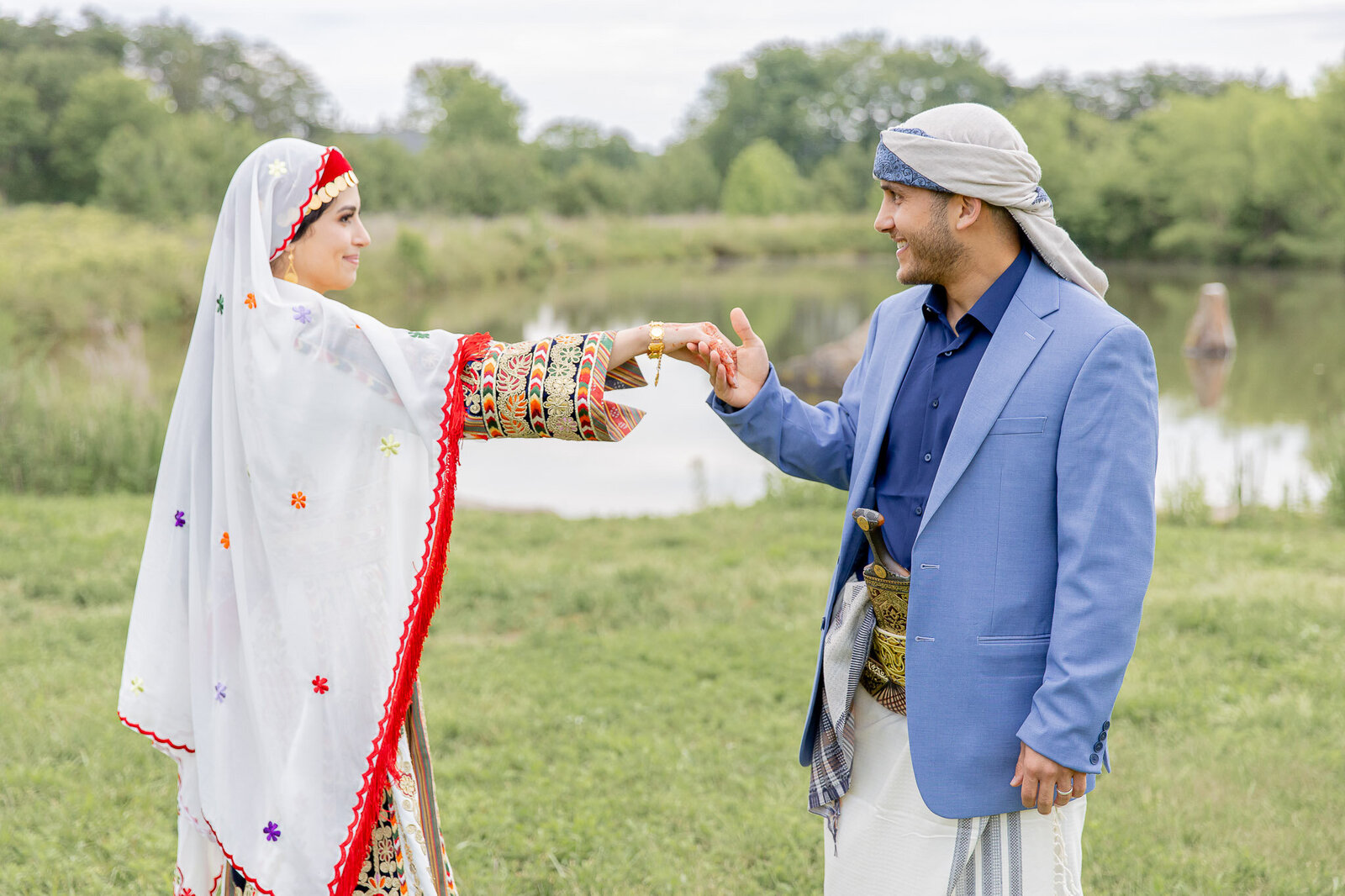 A groom gently holds the hand of his bride. They are outside DC and dressed in traditional Palestinian dress.