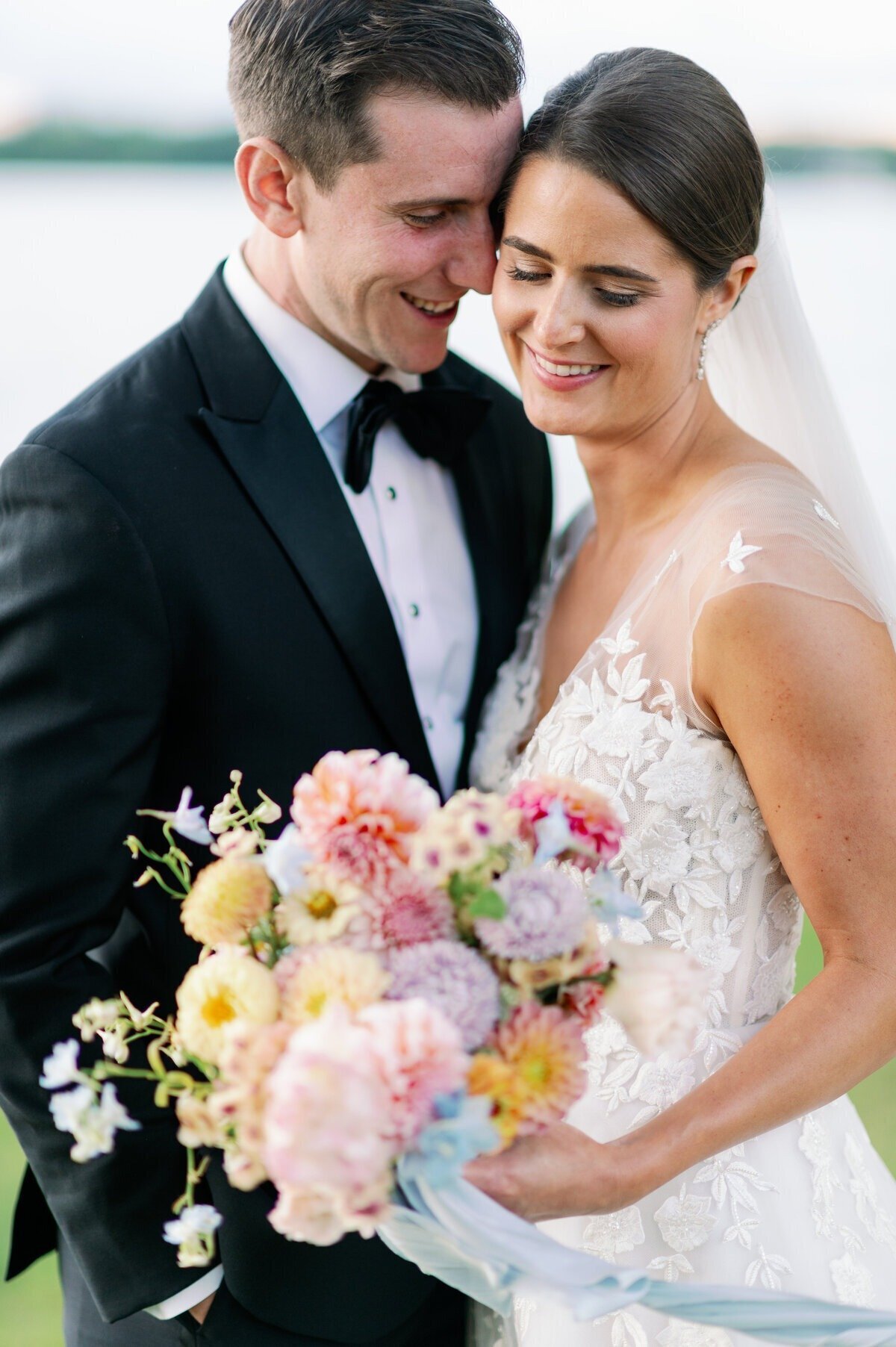 groom embraces bride who looks down at colorful pastel bouquet for their minneapolis wedding day 